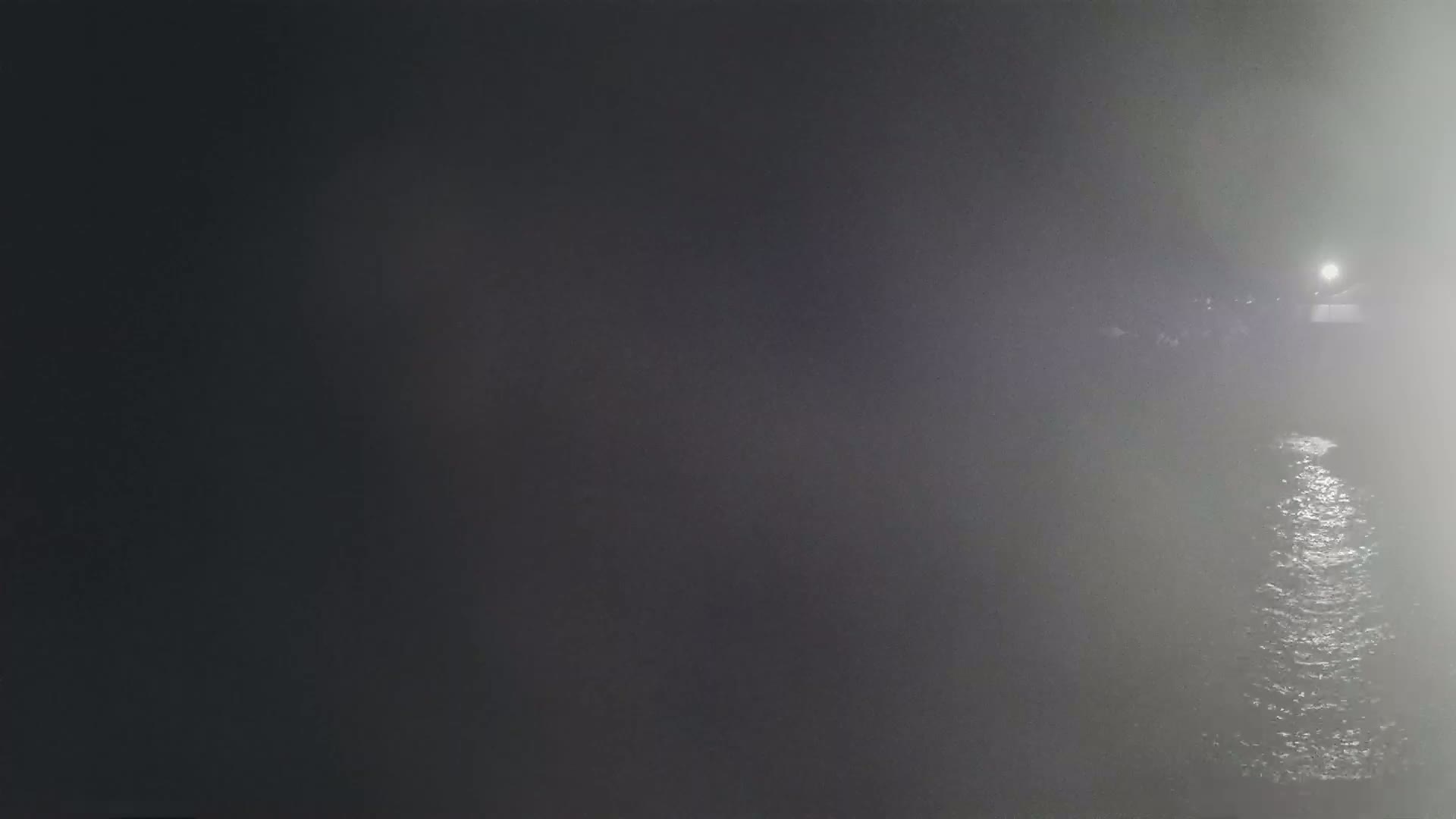 A foggy night scene shows a body of water reflecting a distant light source.