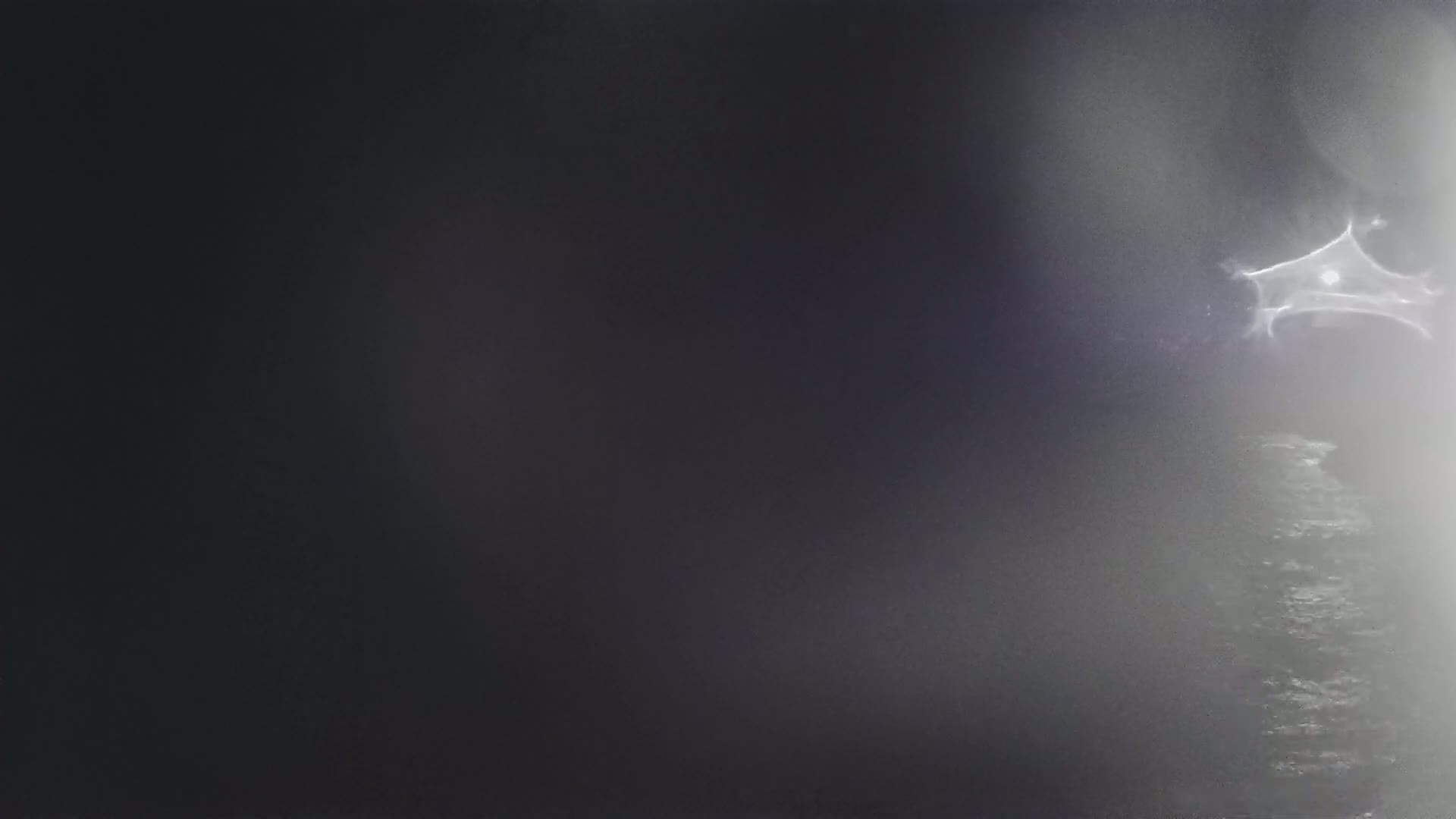 A blurry, dark image shows a bright, star-shaped light source in a foggy or misty atmosphere over a dark body of water.