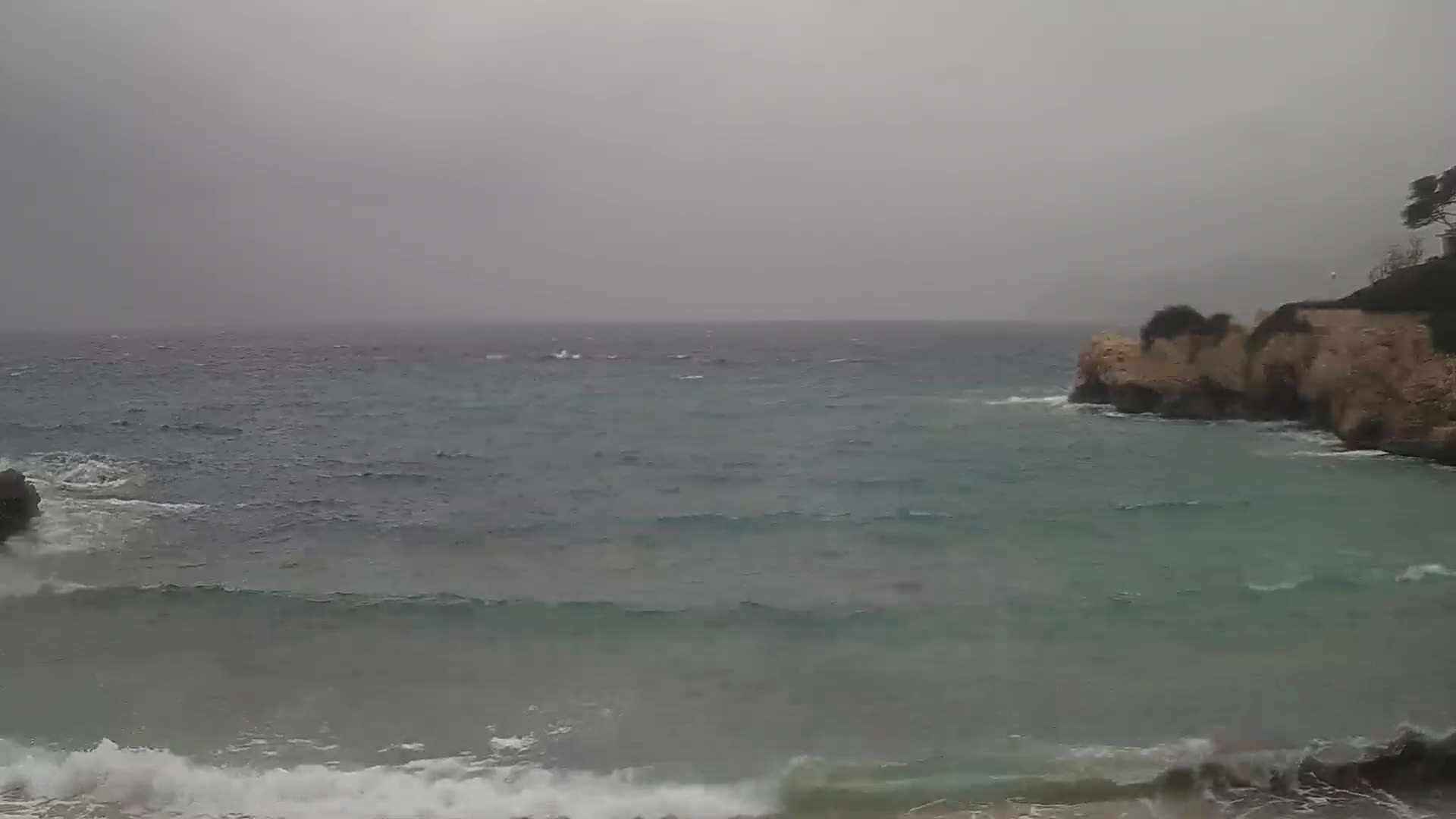 Waves crash against a rocky shoreline on an overcast day.