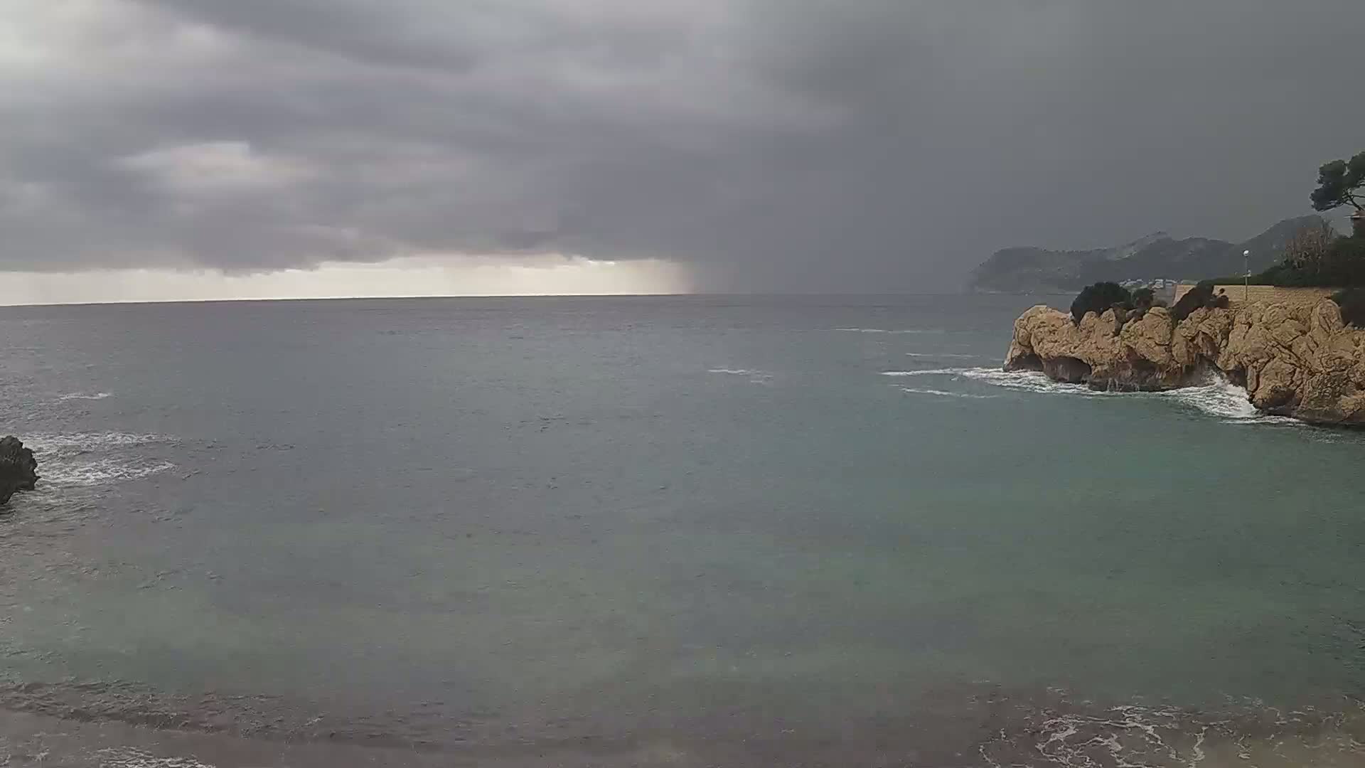 A stormy sea scene shows dark, overcast skies with rain falling over the water, along with rocky cliffs and a coastline.