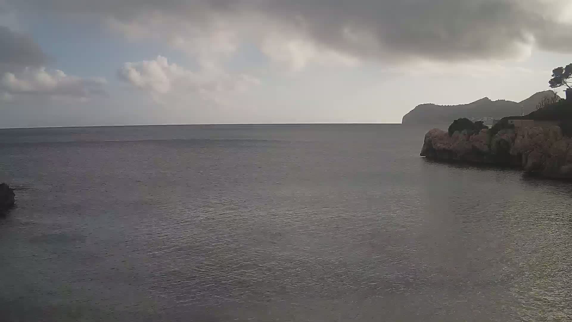 A calm sea stretches to a distant, mountainous shoreline under a cloudy sky.