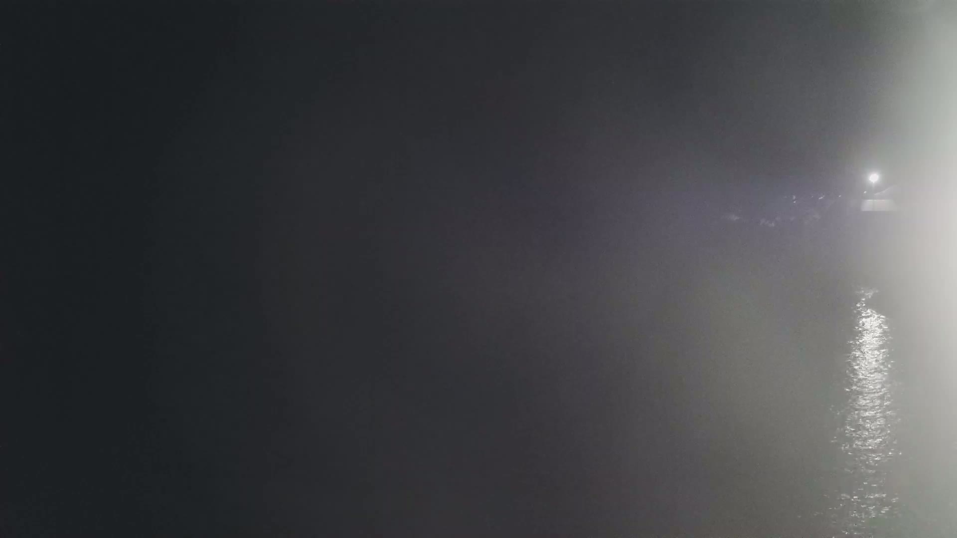 A dimly lit body of water is shrouded in fog at night, with a light source visible in the distance.