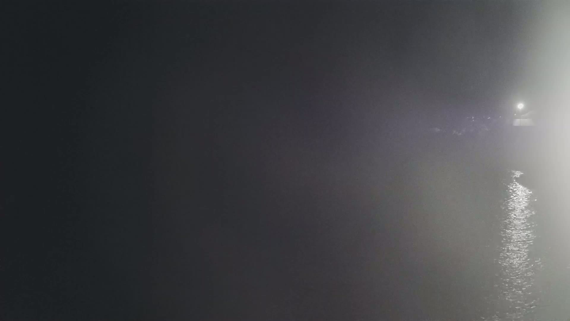 A dimly lit body of water reflects light at night in foggy conditions.