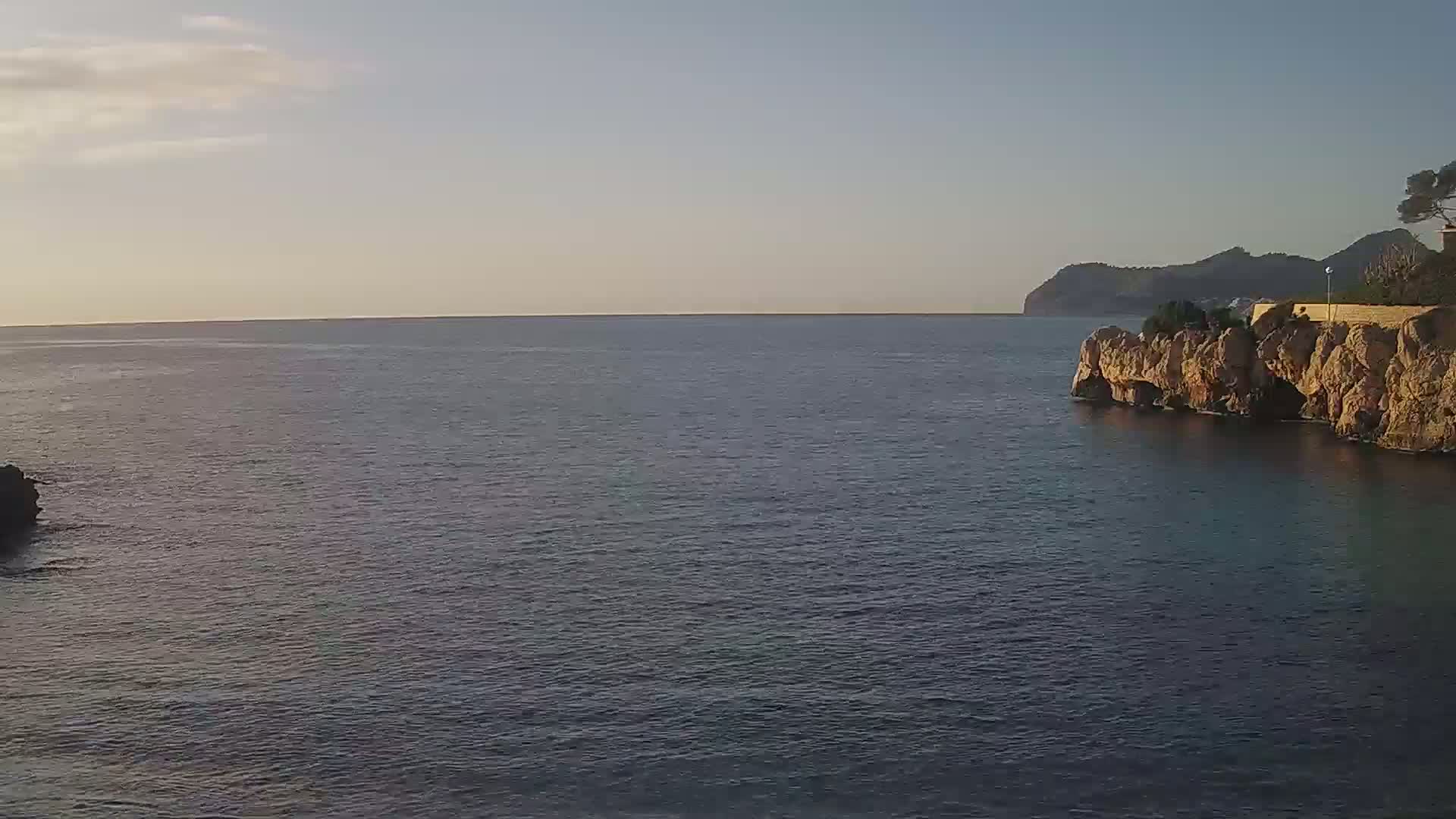 A calm sea stretches to a distant mountain range under a clear, bright sky.