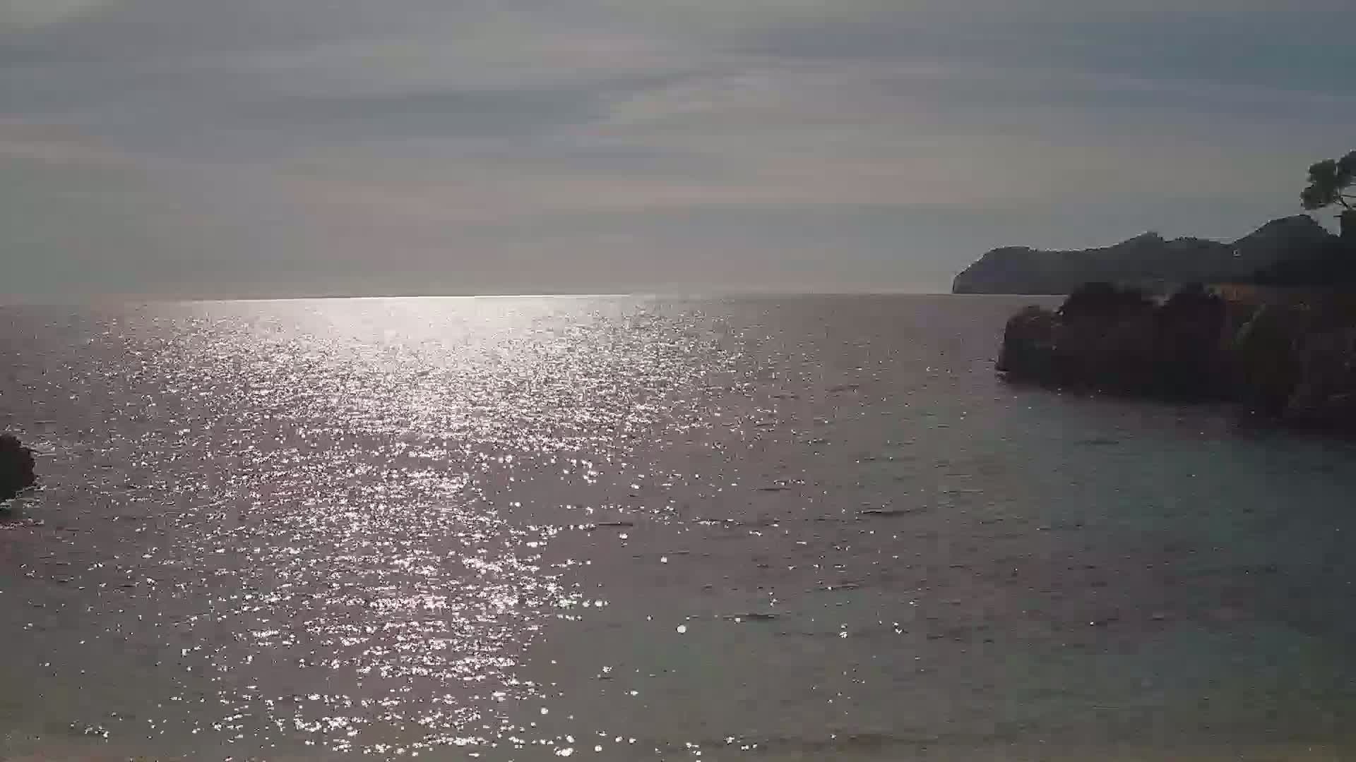 Sparkling water reflects sunlight under an overcast sky, with dark landmasses visible on the horizon and closer to the viewer.