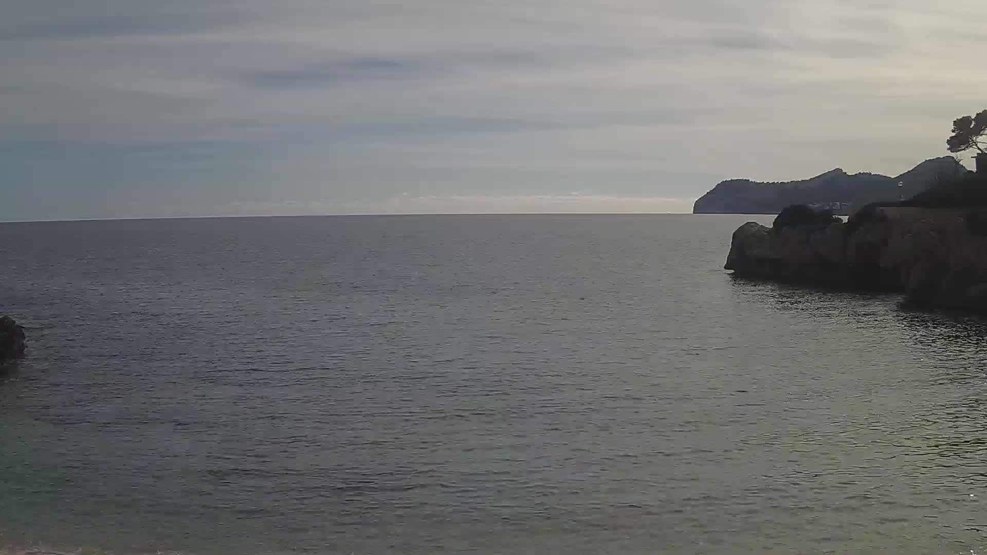 Dark gray-blue calm water laps against rocky shorelines under a cloudy sky, with a distant landmass visible on the horizon.