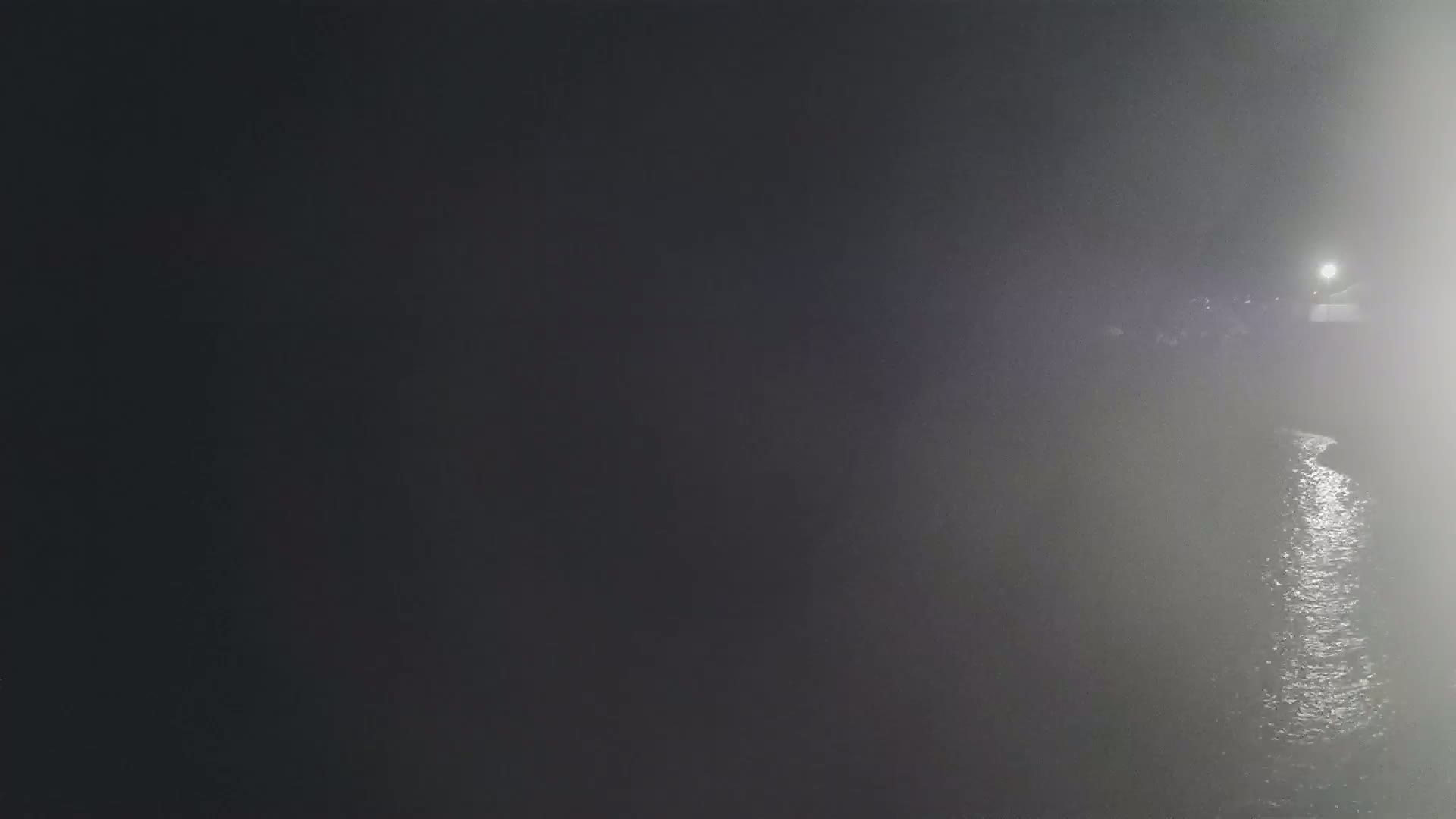 A body of water is visible at night in foggy conditions, with a faint light source in the distance.