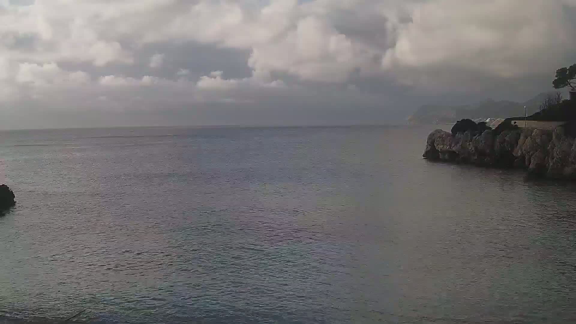 A calm, grey sea is seen under a cloudy sky, with rocky coastlines on either side of the frame.