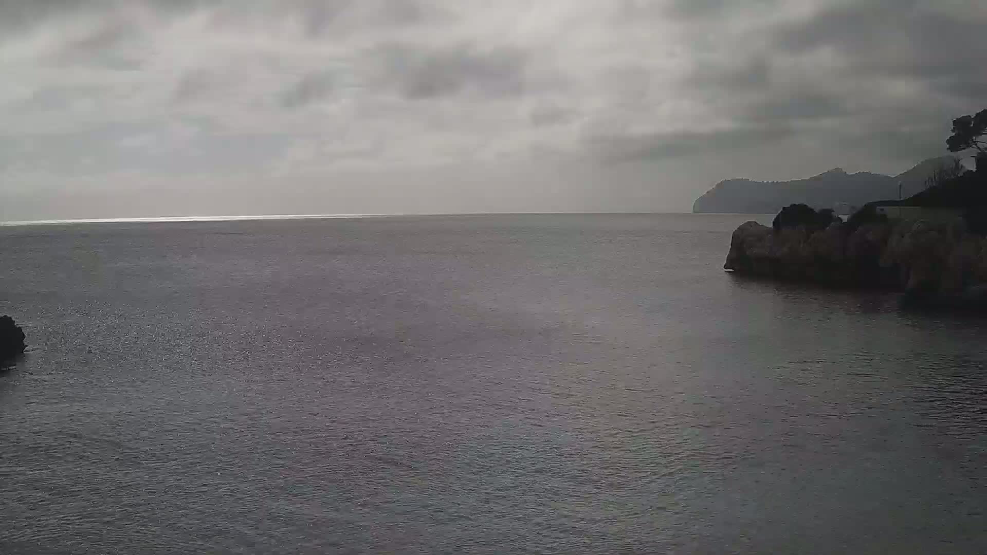 A calm, gray sea stretches to a distant, hazy coastline under an overcast sky.