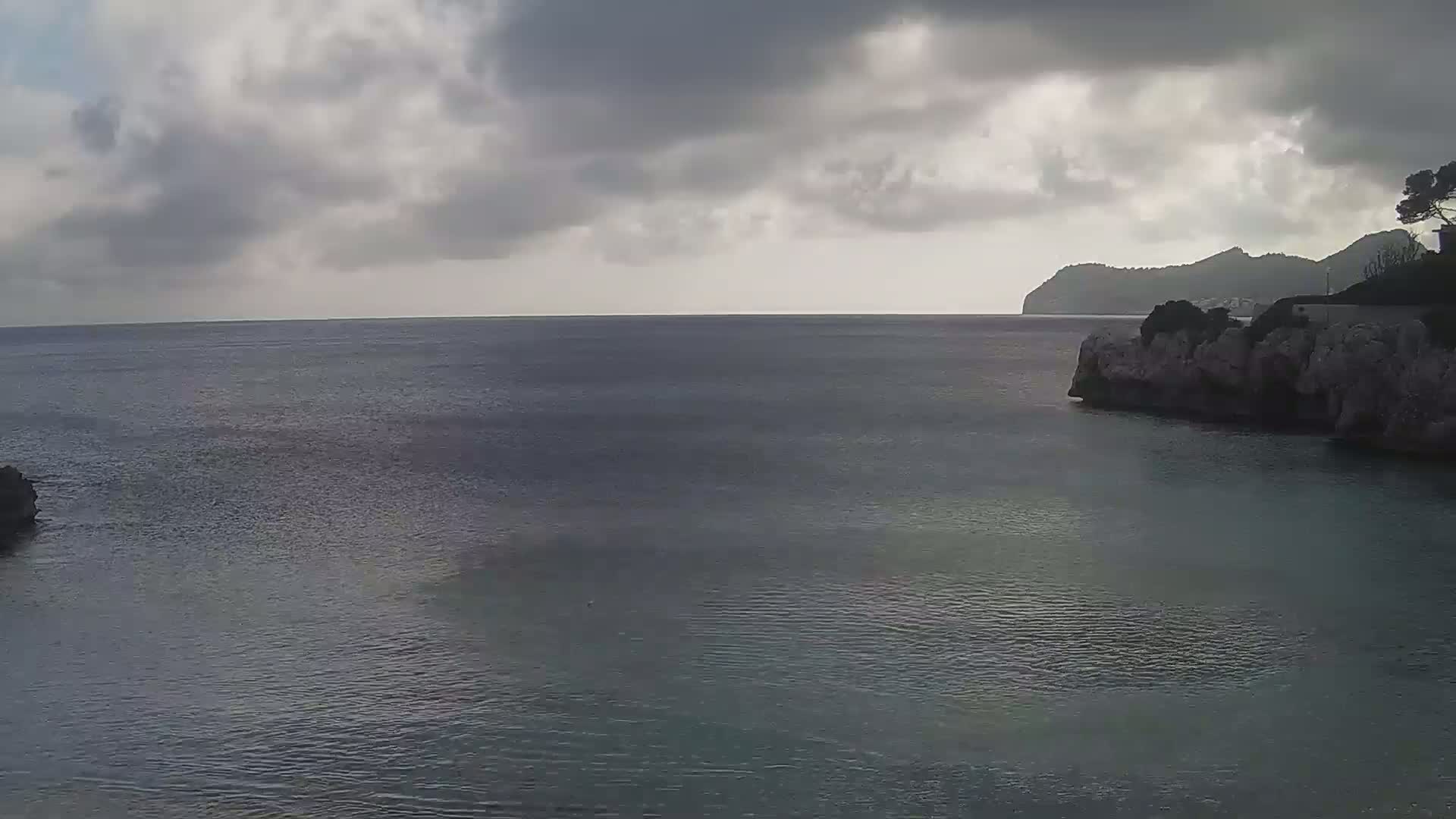 A calm sea is partially enclosed by rocky cliffs under a cloudy sky.