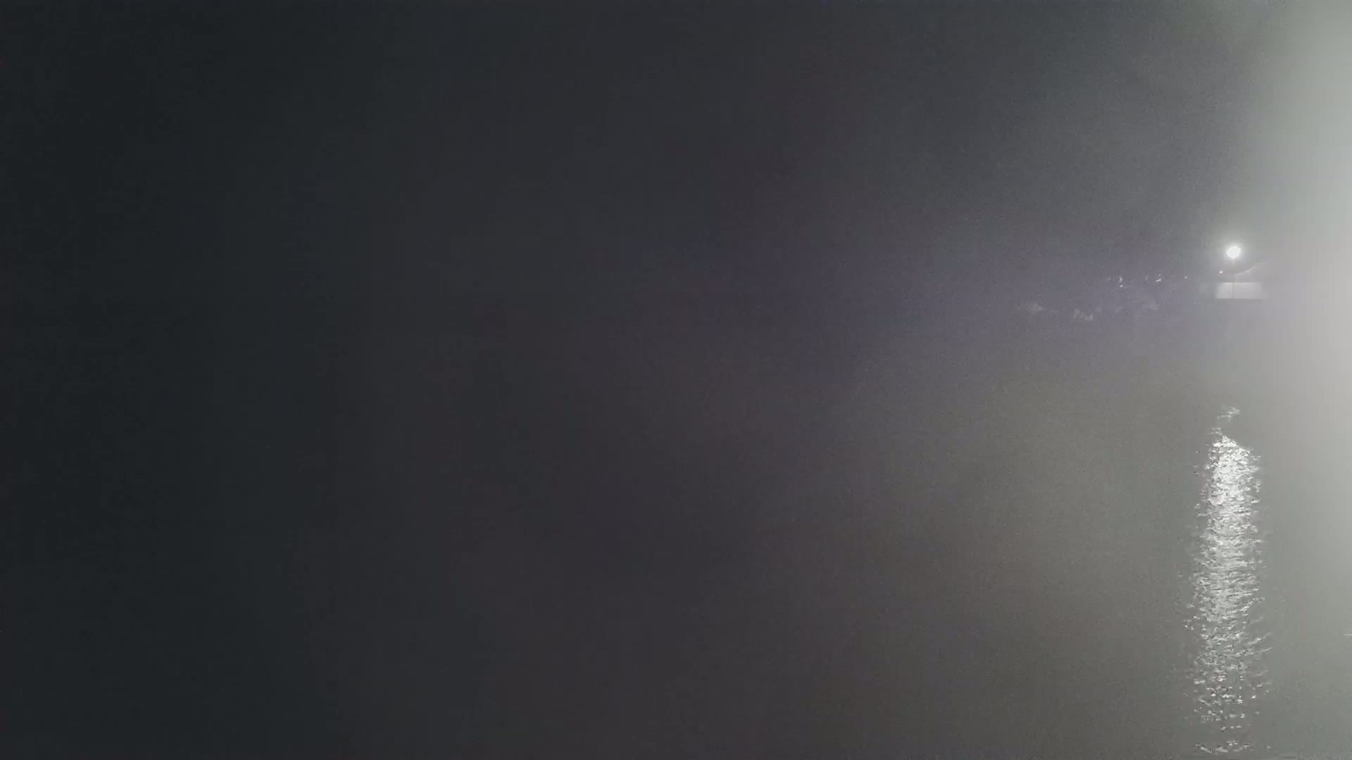A brightly lit area is visible on a foggy body of water at night.