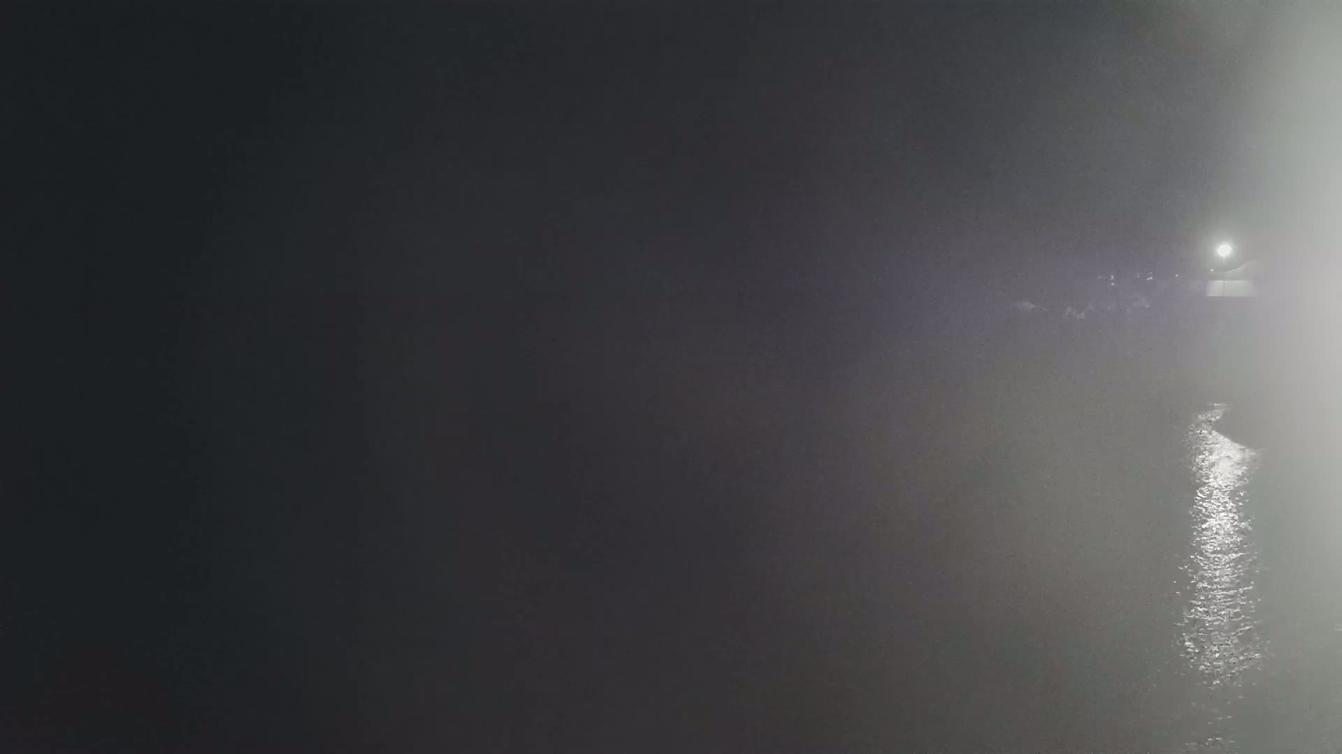 A dimly lit body of water is visible through a thick fog at night, with a single light source in the distance.