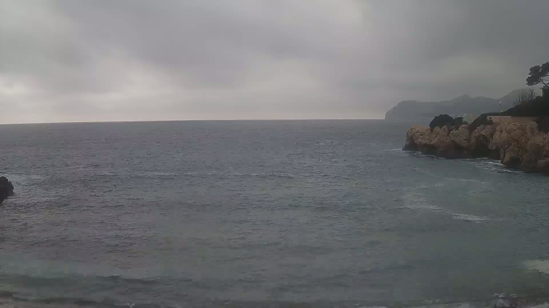 A gray, overcast sky hangs over a choppy sea meeting a rocky shoreline.