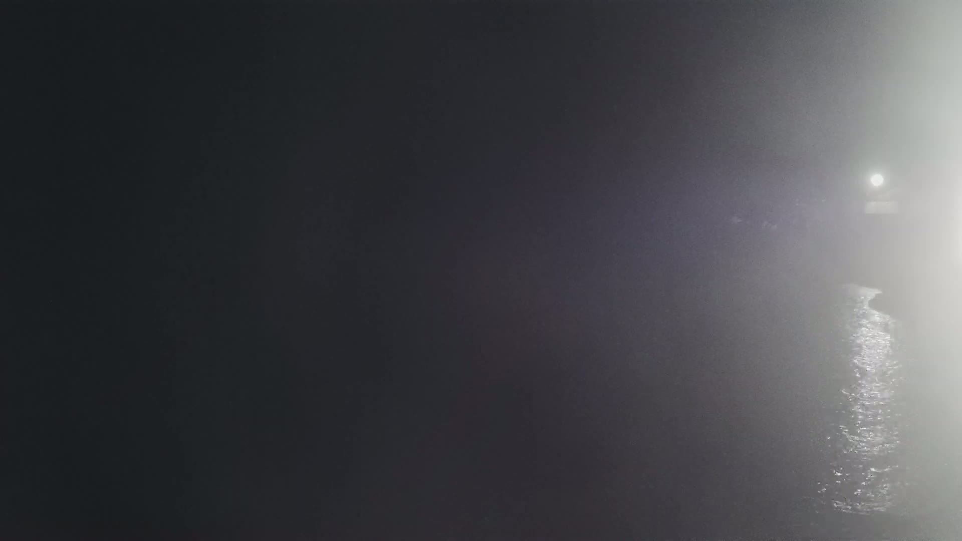 A dimly lit body of water is shrouded in fog, with a light source visible in the distance.