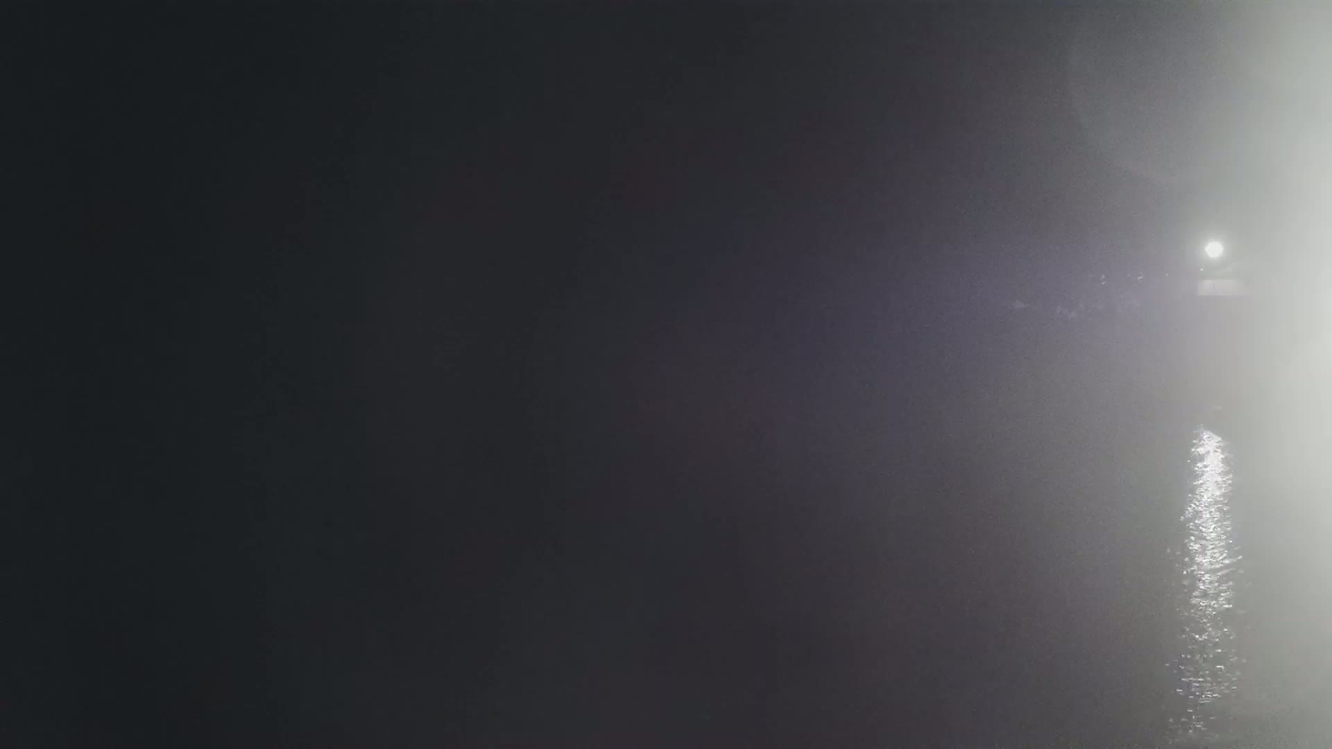 A bright light shines over a dark, foggy body of water at night.
