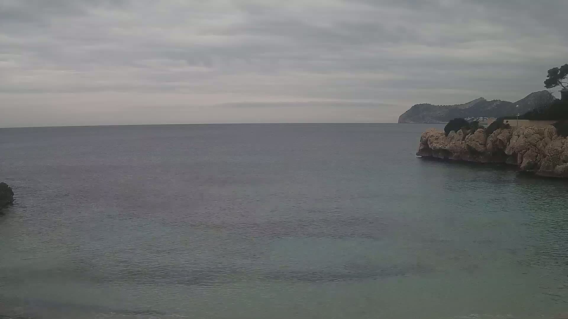 A calm, gray-toned sea stretches to a distant, mountainous coastline under an overcast sky.