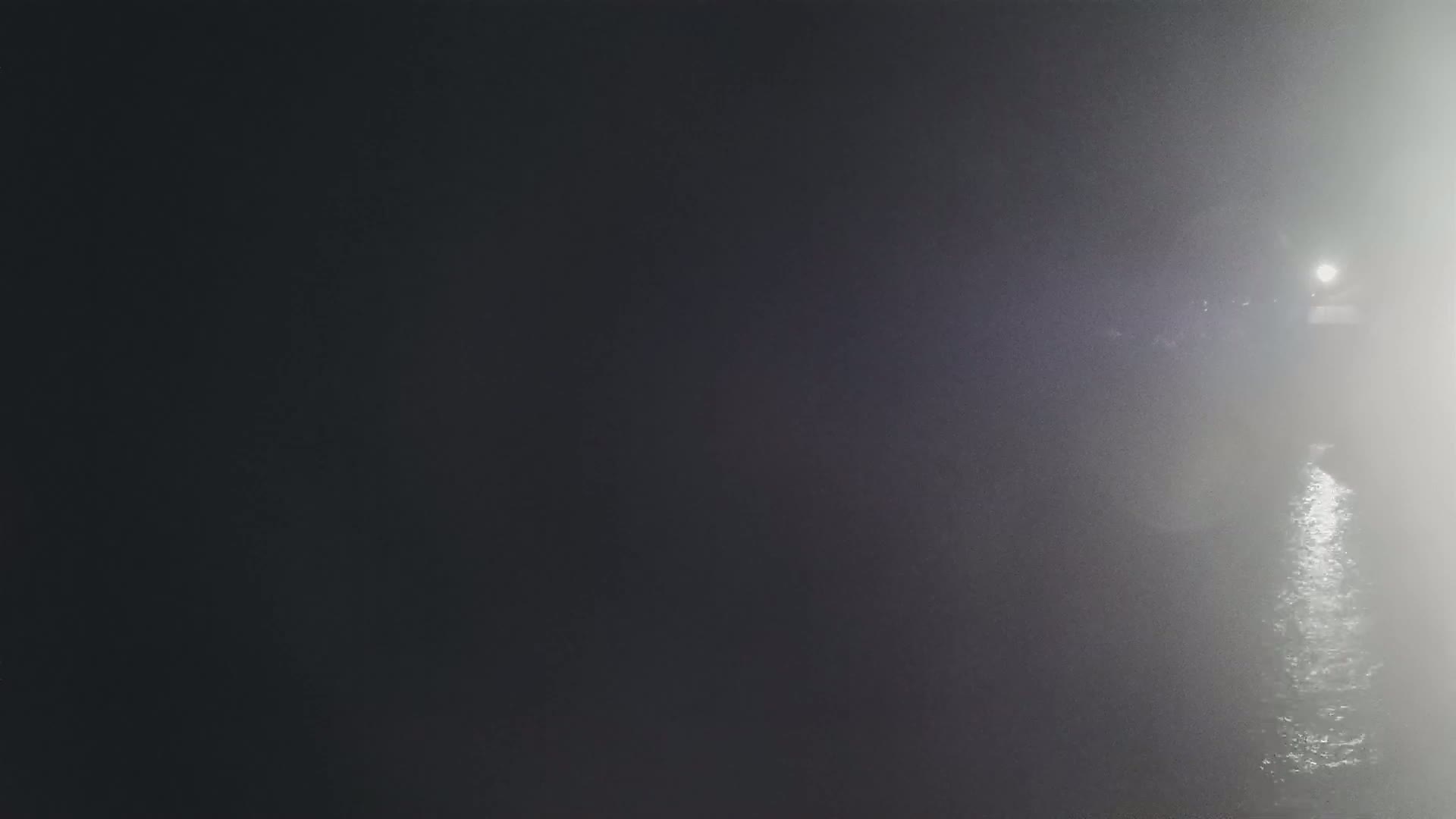 A bright light illuminates a foggy night scene over dark water.