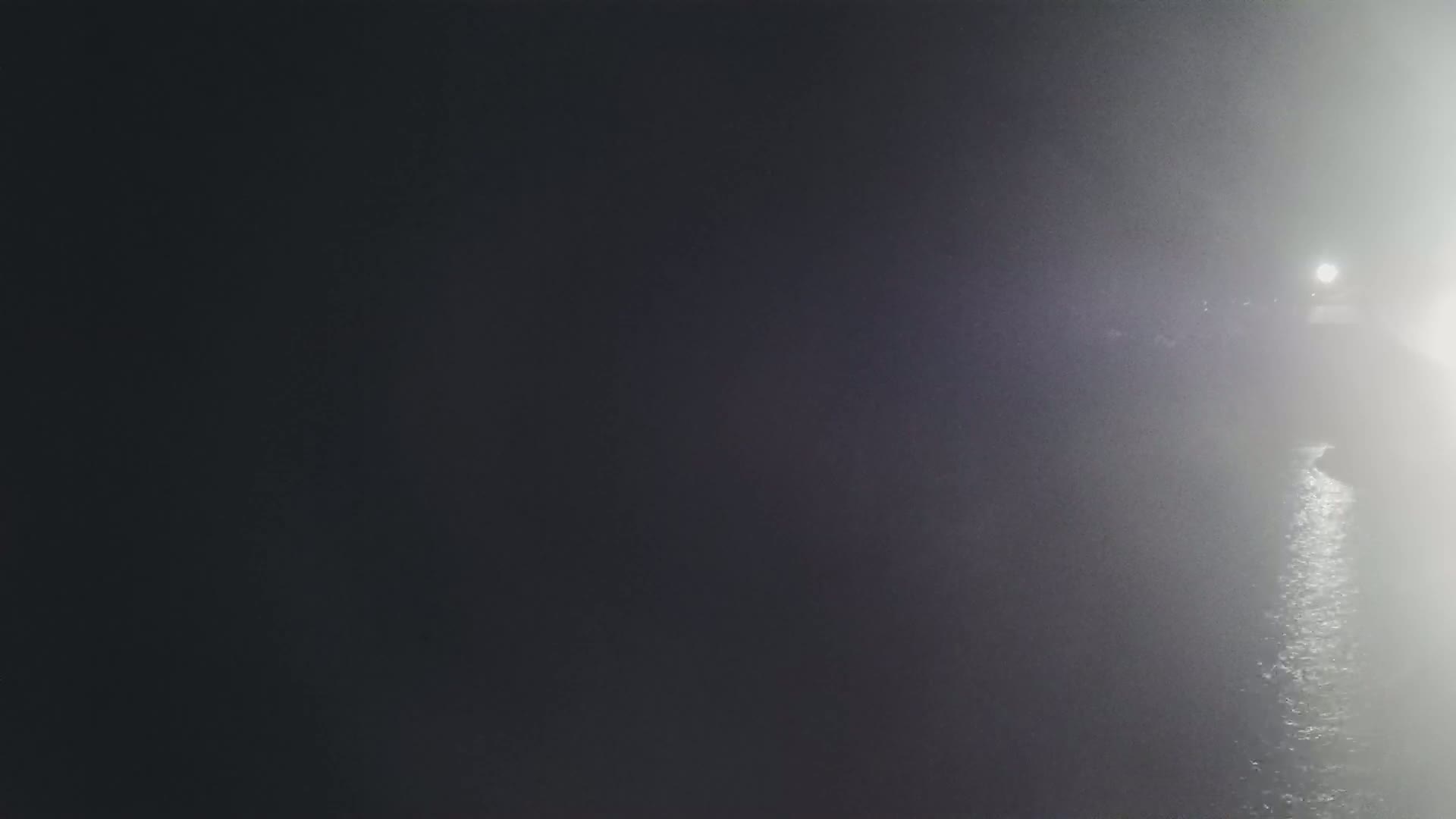 A brightly lit area is visible in the distance through a thick fog at night.