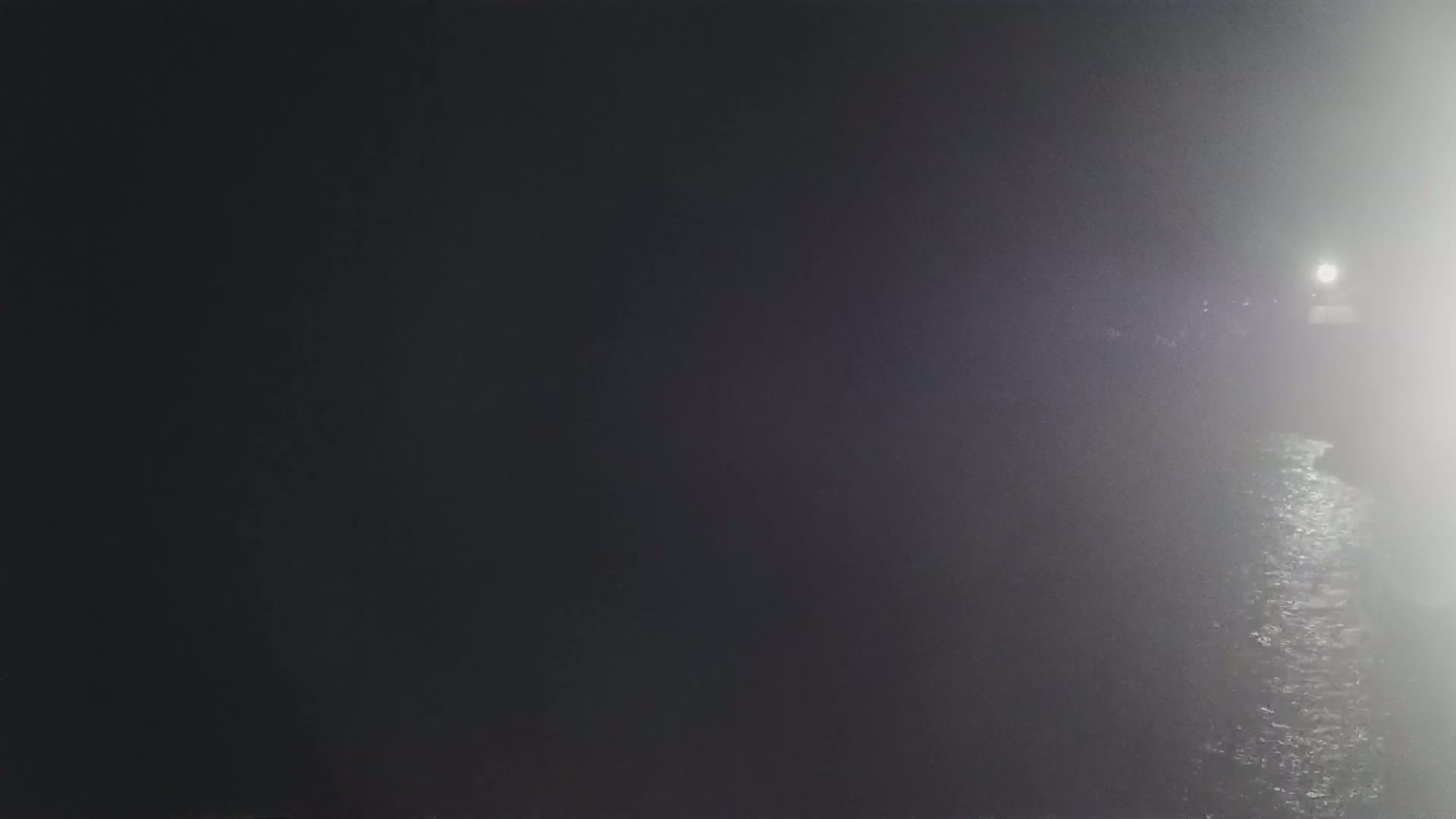 A dimly lit body of water is visible through a heavy fog at night.