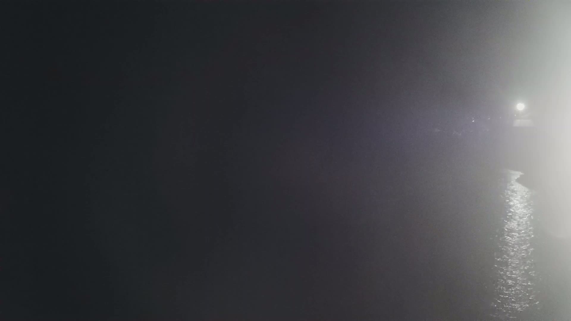 A foggy night scene shows a body of water reflecting light from a distant source.