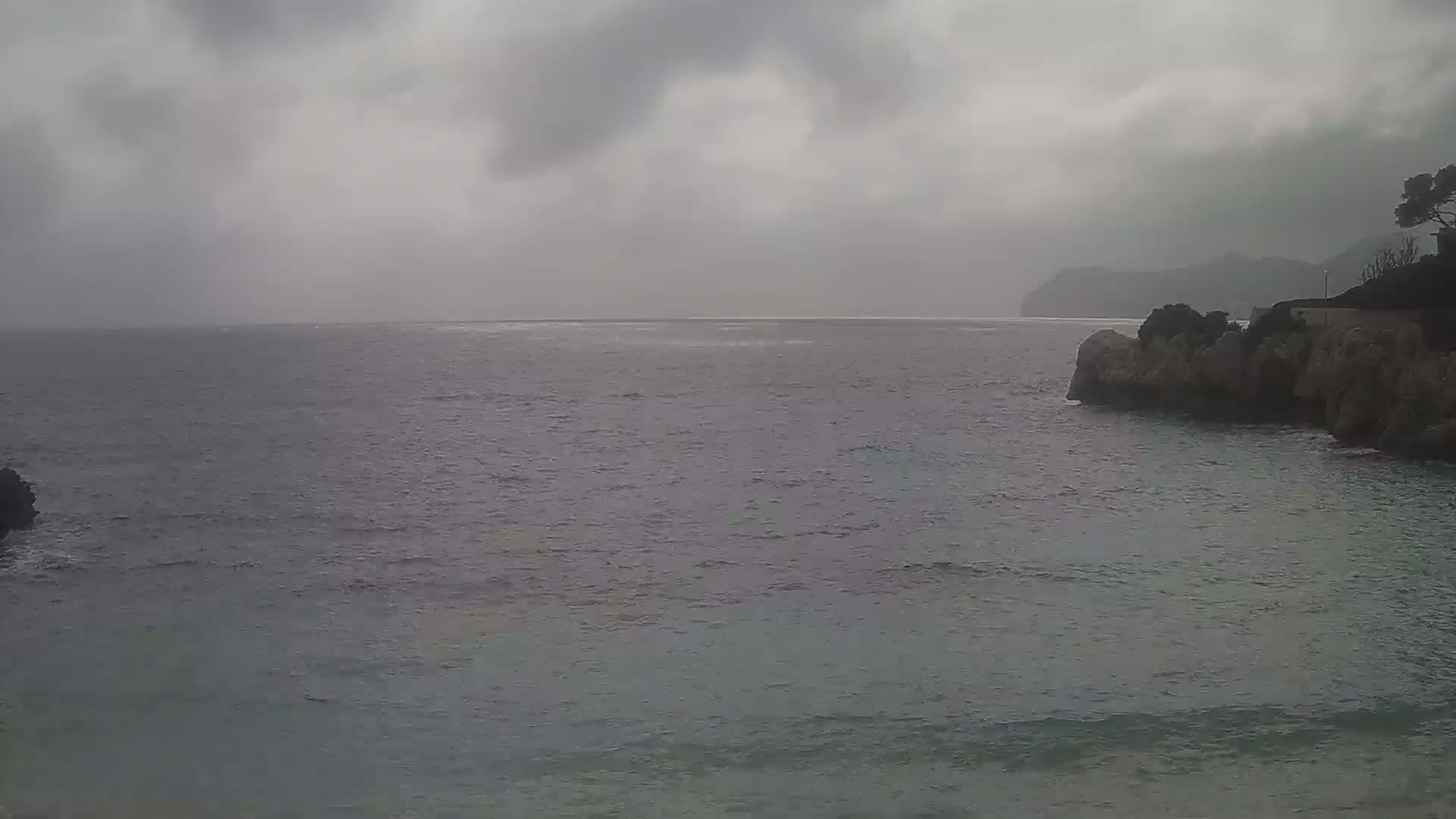 A dark, overcast day shows a choppy sea meeting rocky shorelines under a gray sky.