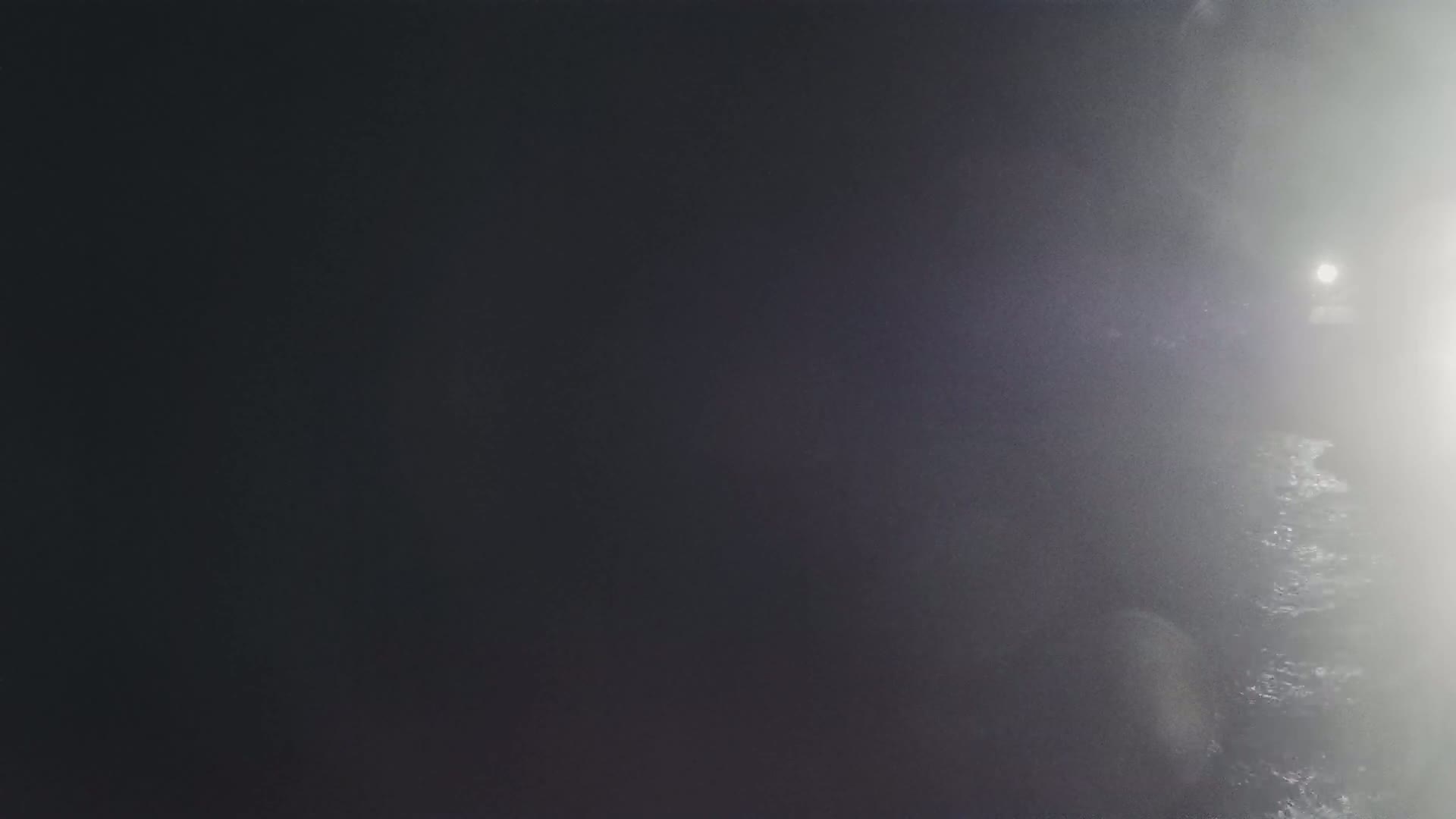 A dimly lit, foggy scene shows a dark, possibly wet surface with a bright light source in the distance.