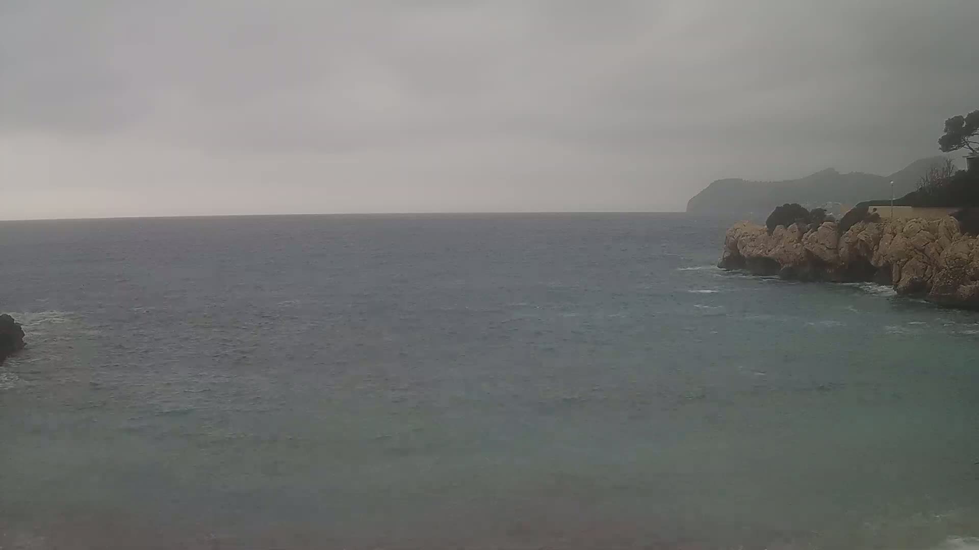 A choppy sea meets a rocky, pale cliff under an overcast sky.