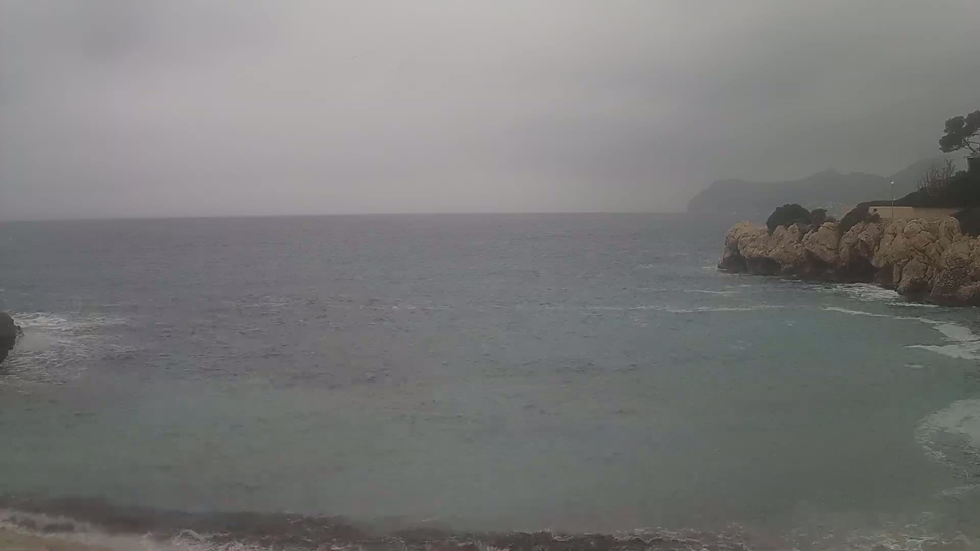 A gray, overcast day shows a rocky coastline meeting a choppy sea under a cloudy sky.