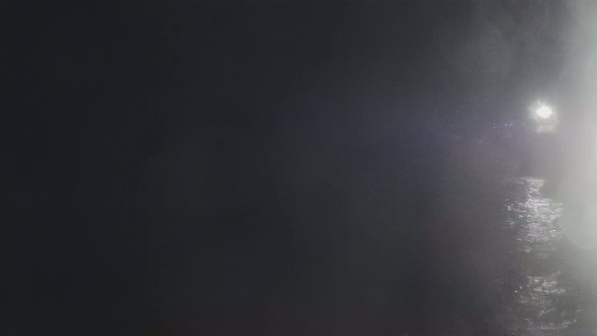 A bright light shines through heavy fog over dark water.