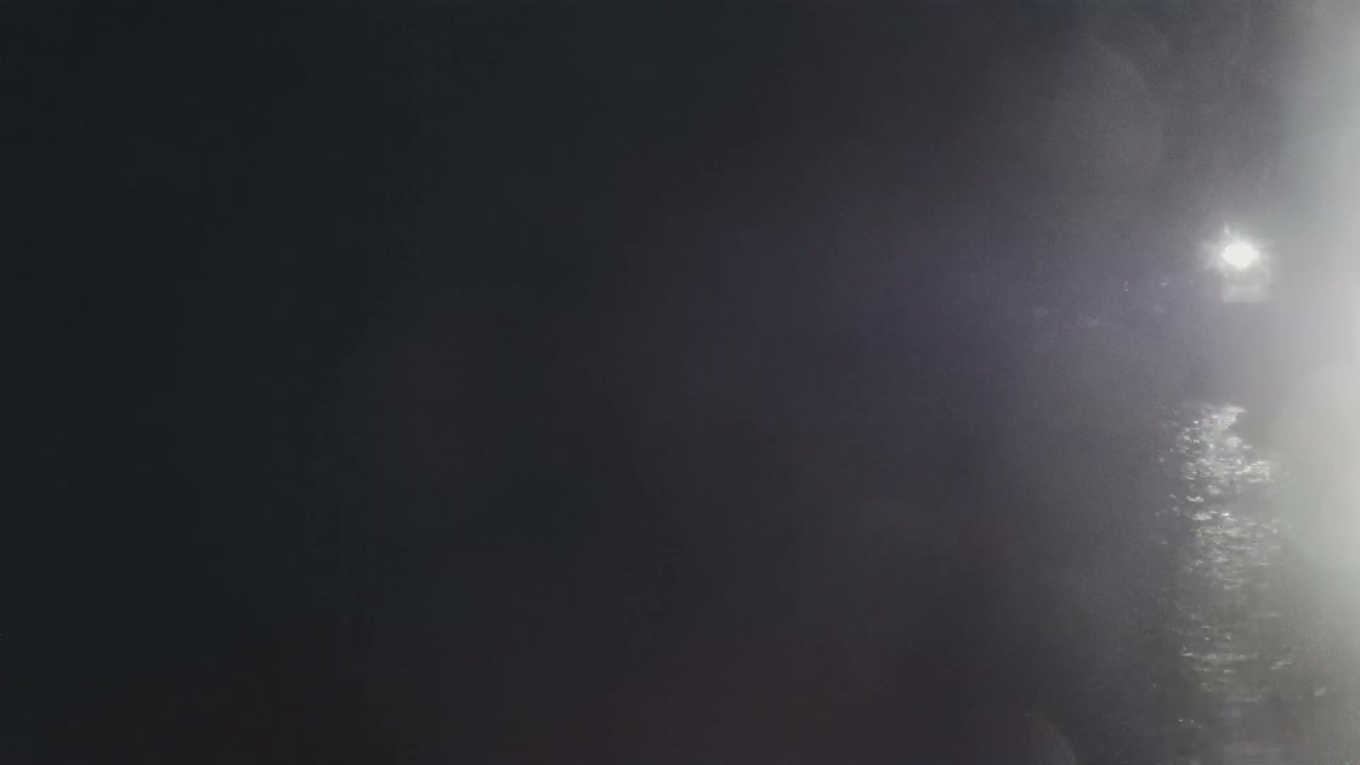 A blurry, dark image shows a bright light in the distance through a hazy or foggy atmosphere.