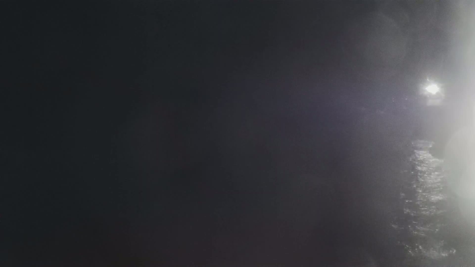 A blurry, nighttime image shows a bright light in the distance through a foggy or misty atmosphere.