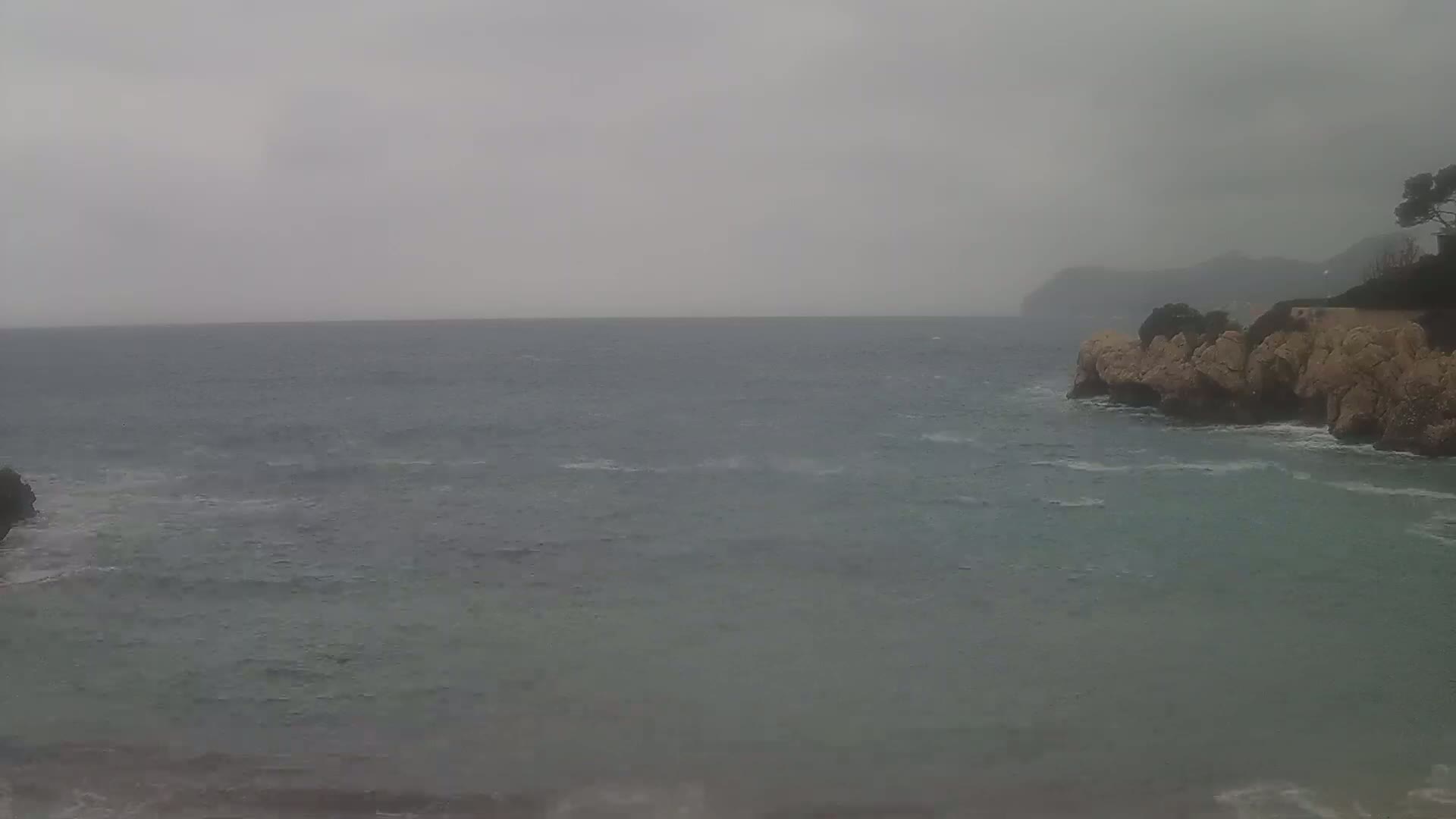 A choppy sea meets a rocky shoreline under an overcast sky.