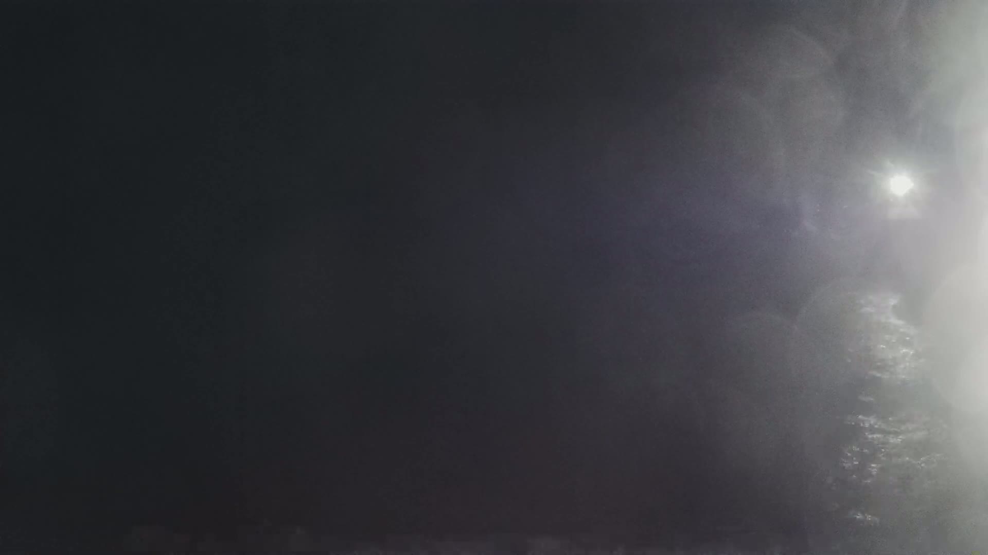A bright light shines through a dense fog or mist at night.