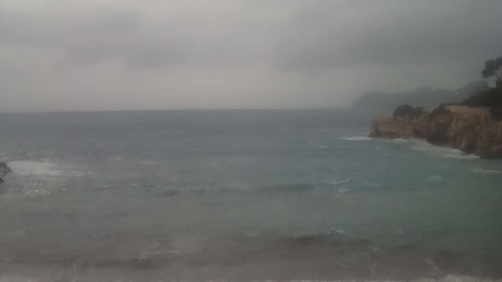 Waves crash against a rocky coastline under an overcast sky.