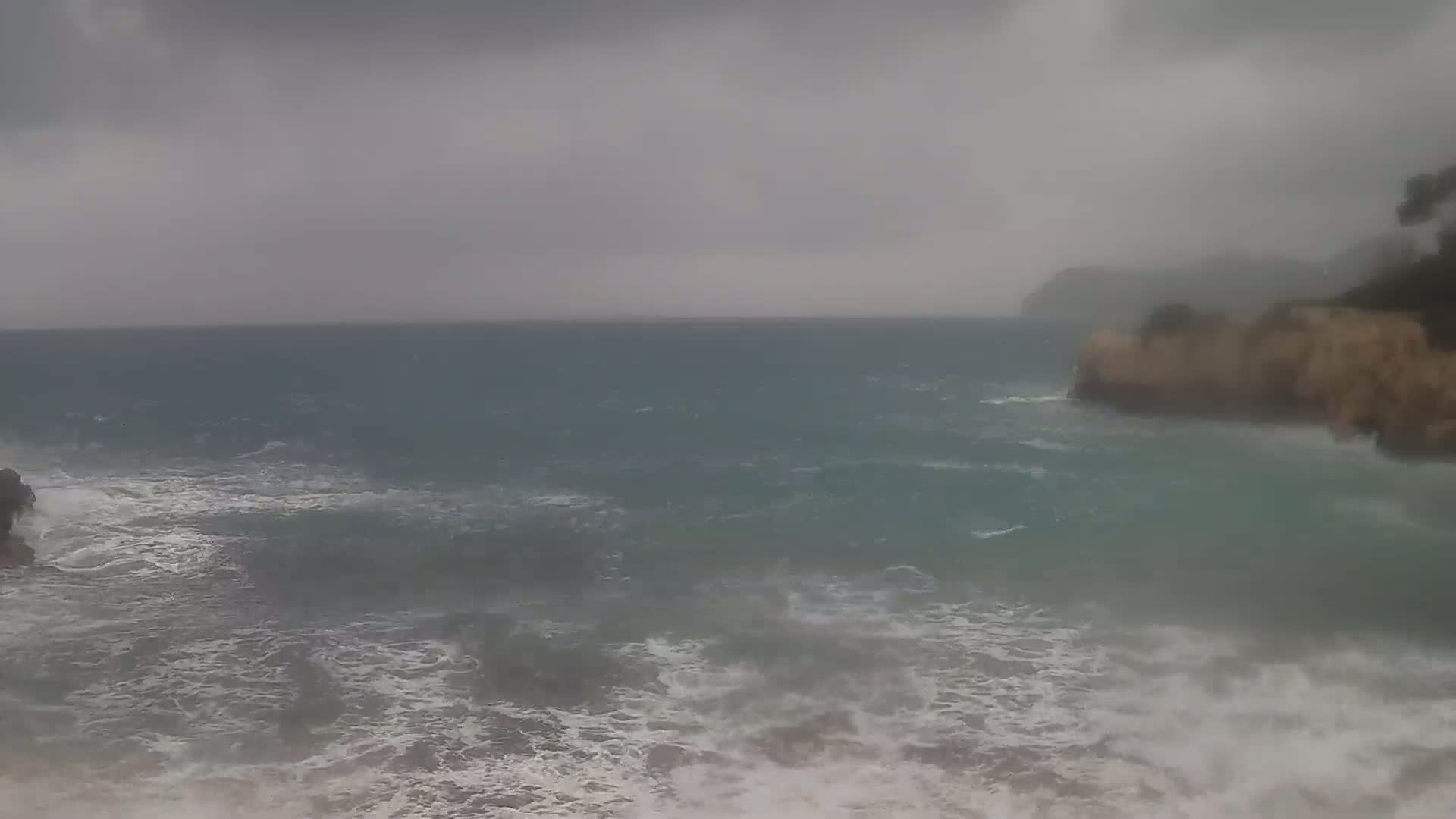 A stormy sea crashes against rocky shores under a gray, overcast sky.