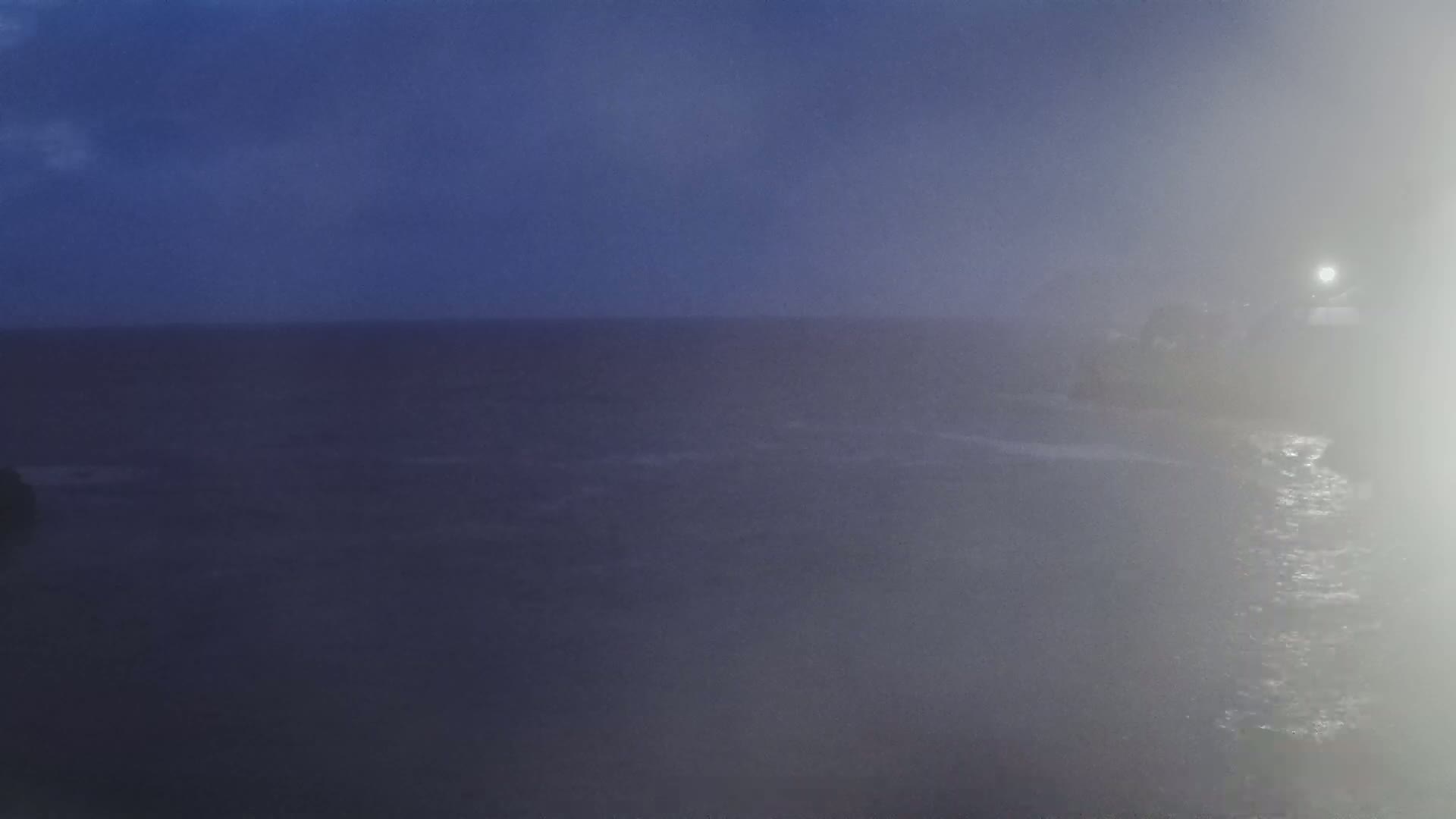 A foggy, dark-blue ocean scene at night shows a distant, dimly lit shoreline.