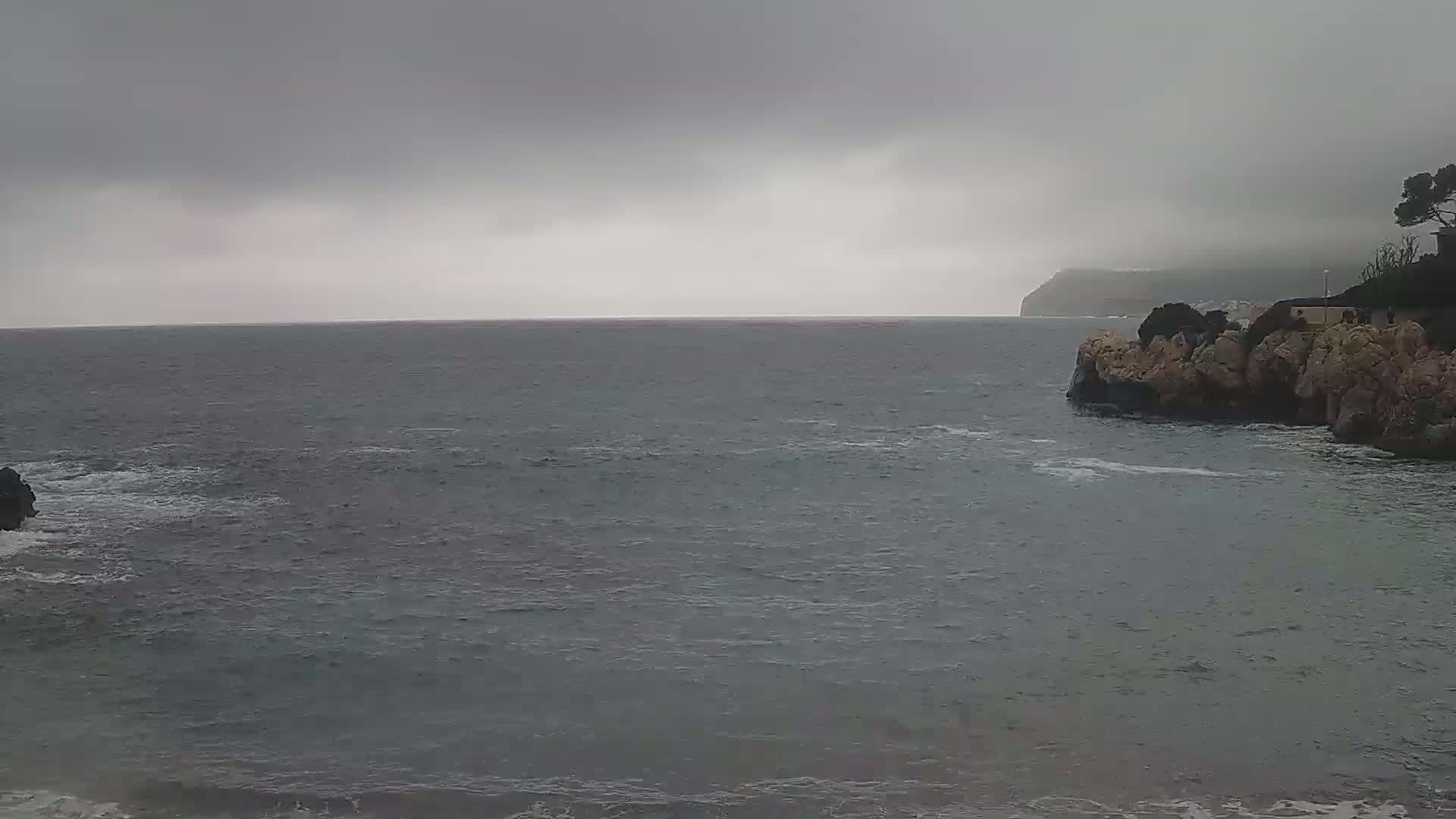 A gray, overcast sky hangs over a choppy sea, where rocky headlands jut into the water.