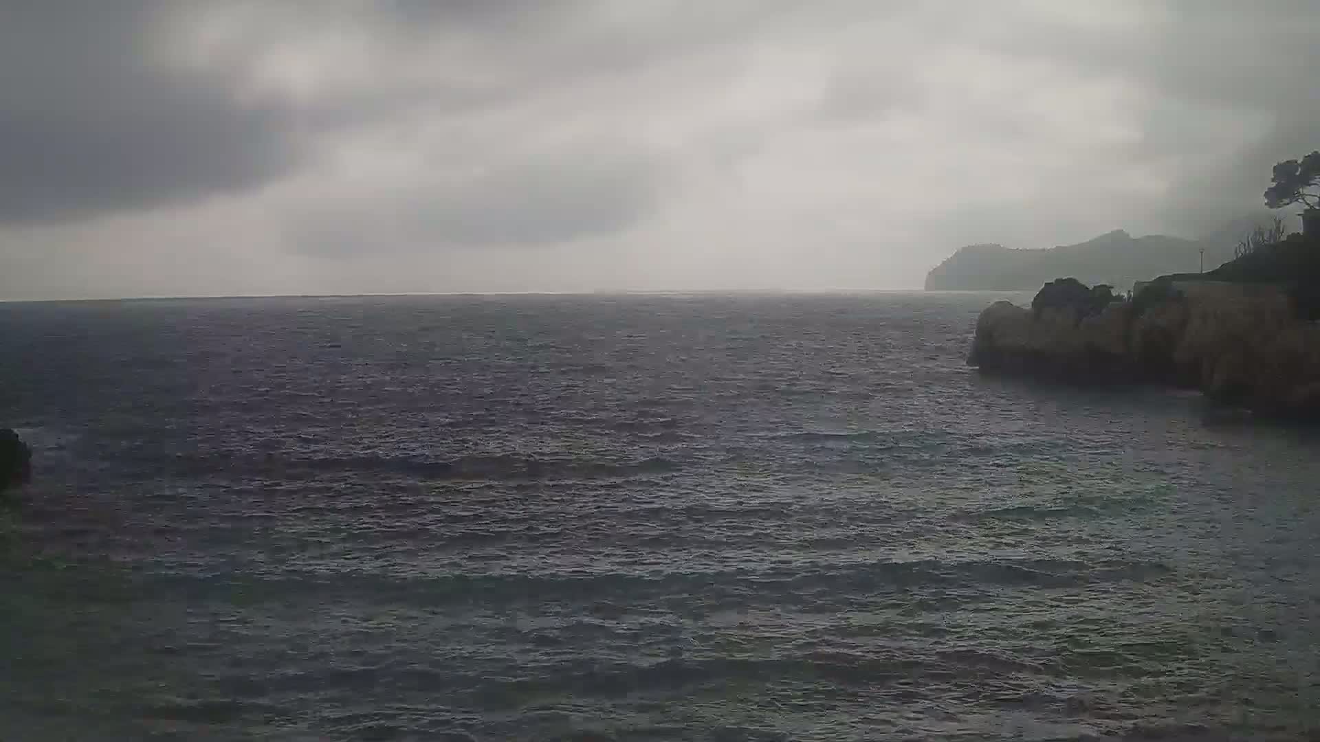 A dark, overcast sky hangs over a choppy sea meeting rocky shores.