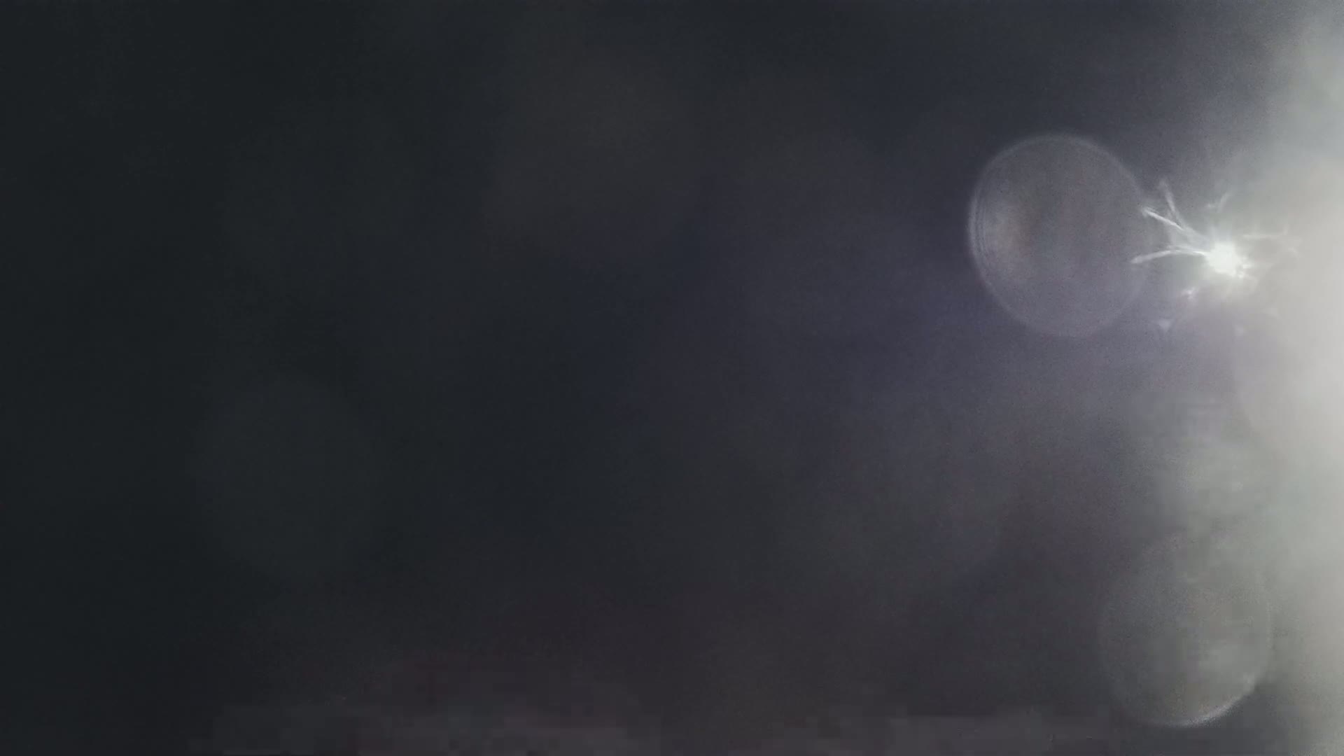 A blurry, dark image features bright, out-of-focus light sources, resembling lens flare.