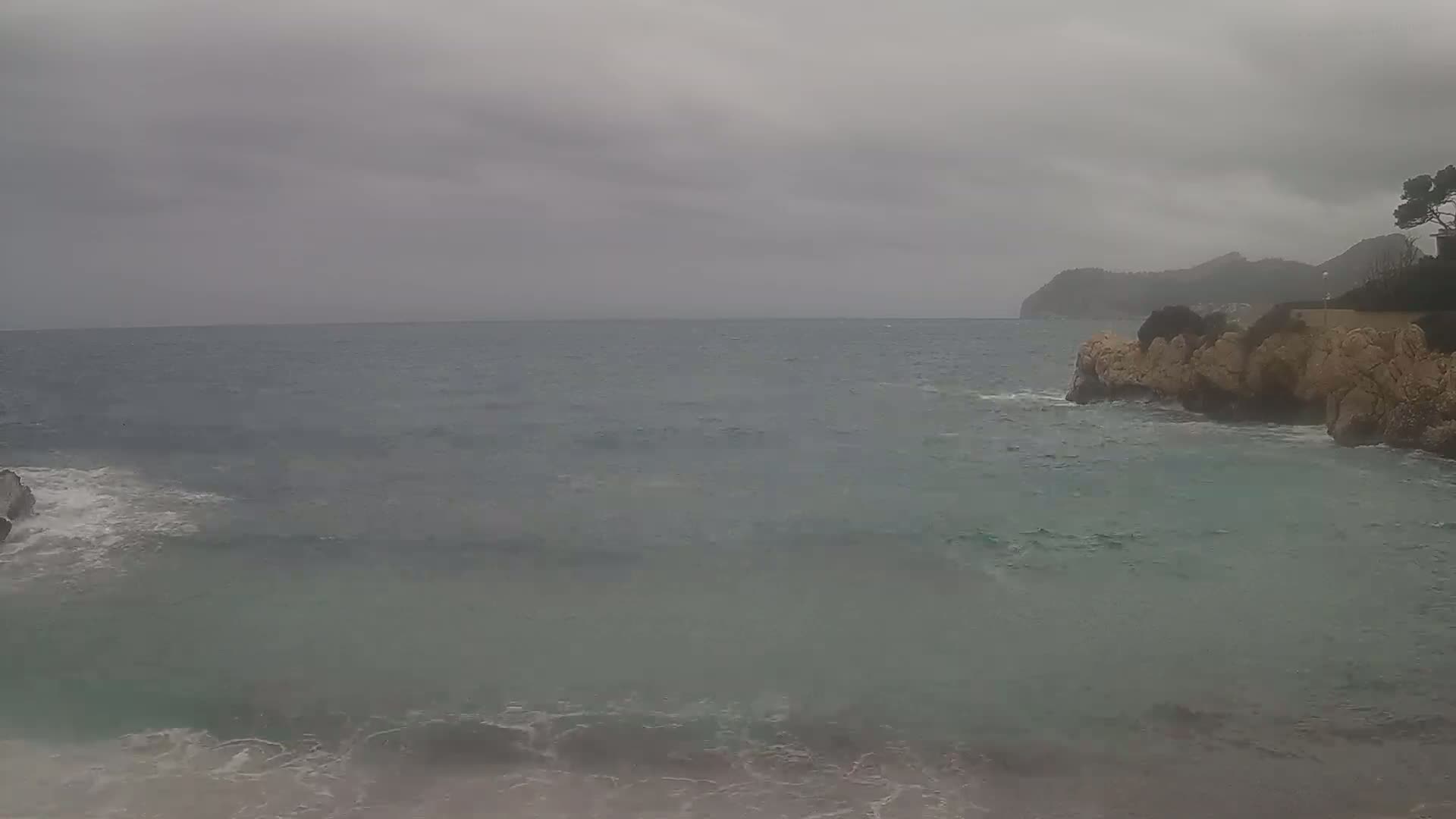 A rocky shoreline meets a choppy sea under a gray, overcast sky.