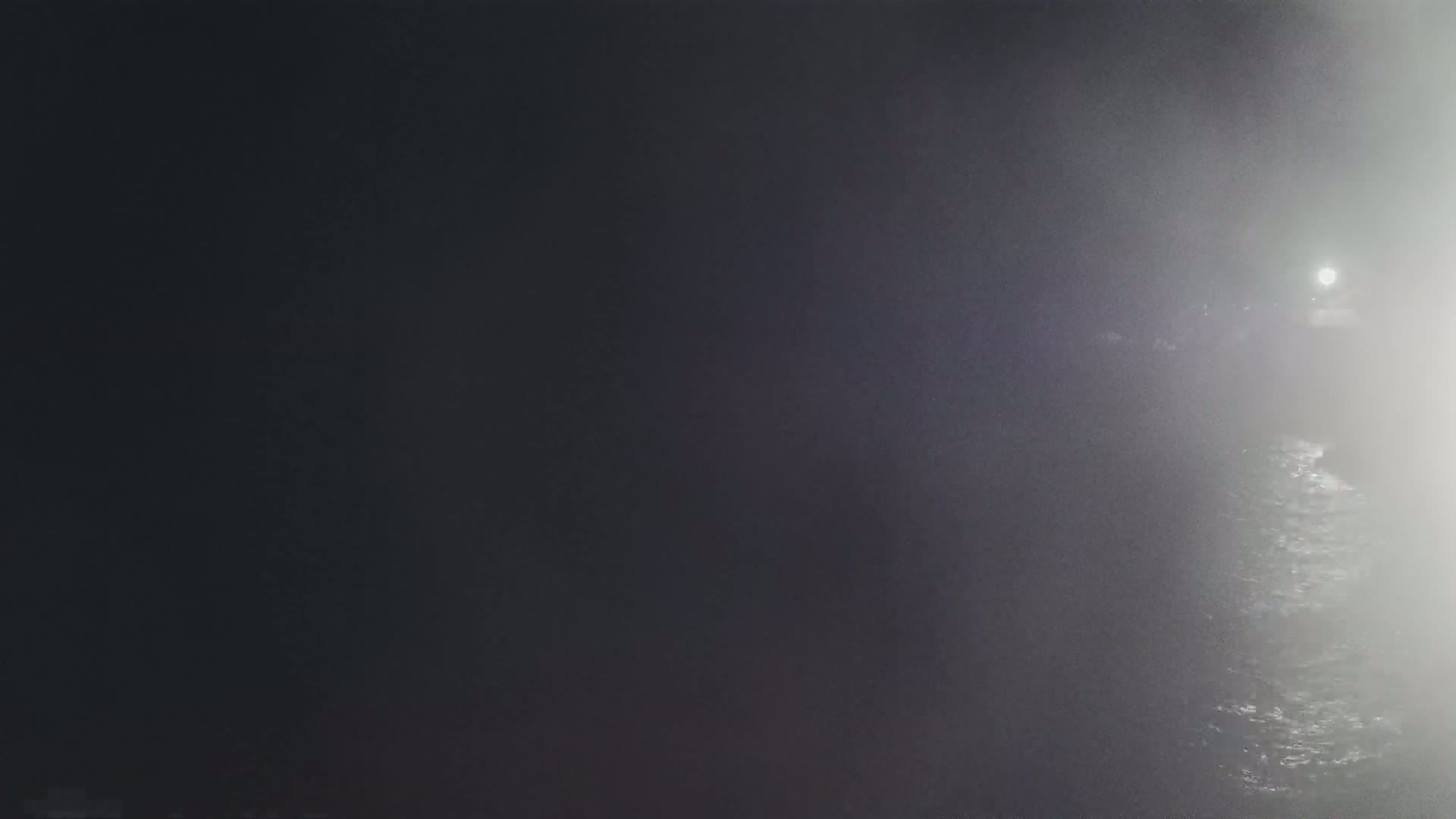 A dimly lit, foggy scene shows dark water with a light source in the distance.