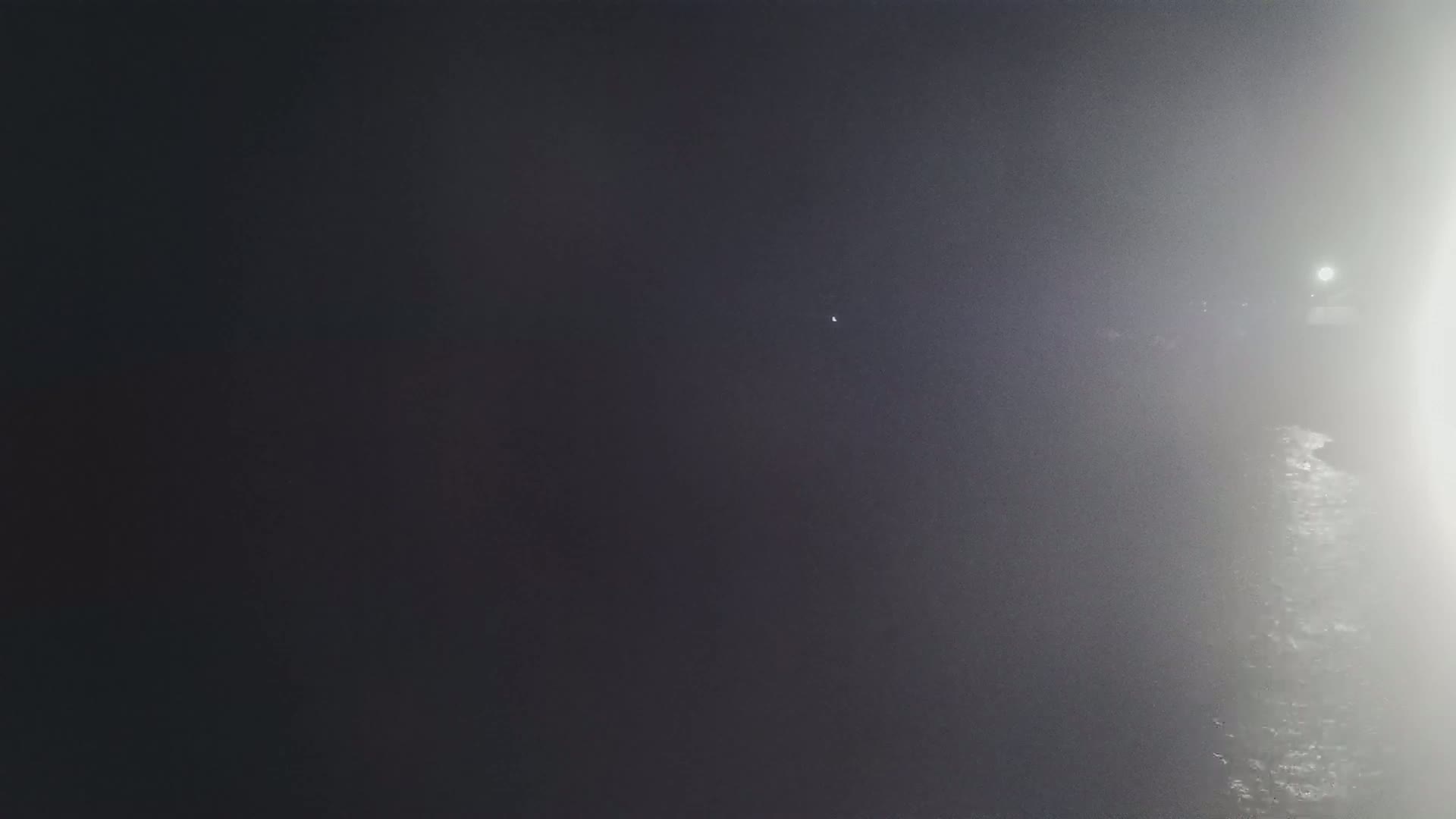 A hazy, dark night scene shows a dimly lit area with a bright light source in the distance.