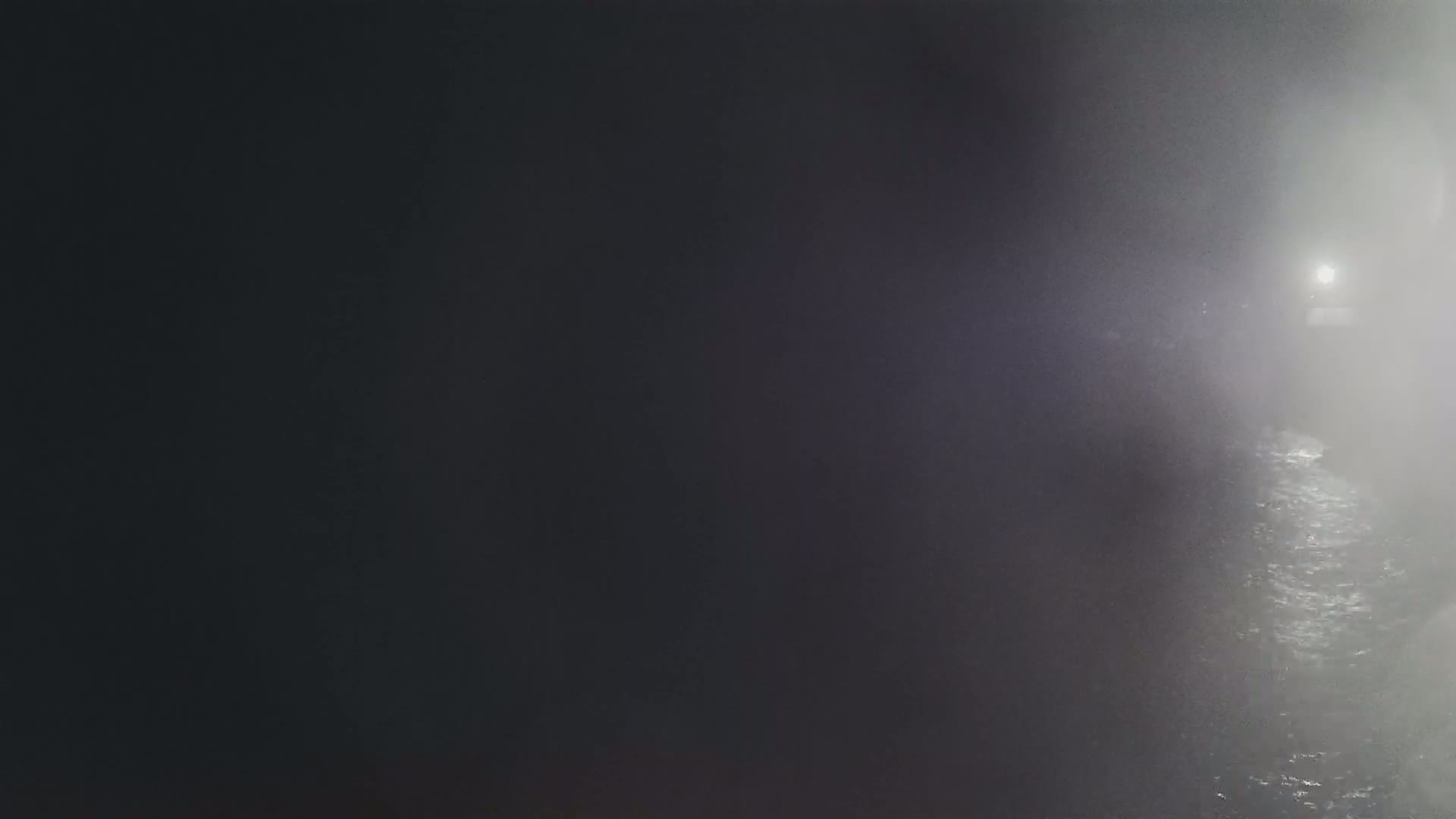 A dimly lit, foggy scene shows a body of water reflecting light from a distant source.
