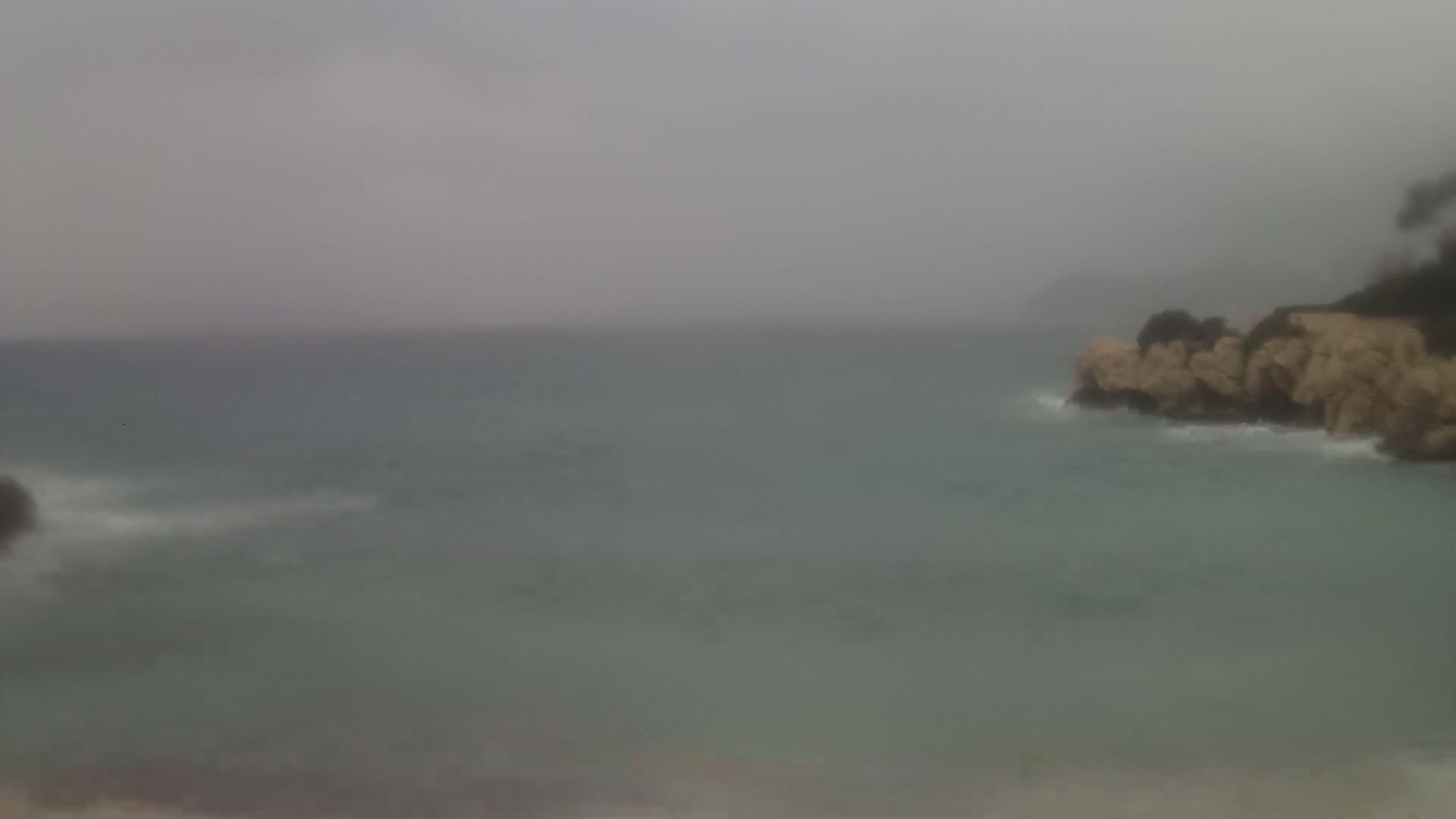 A calm sea meets a rocky shoreline under an overcast sky.