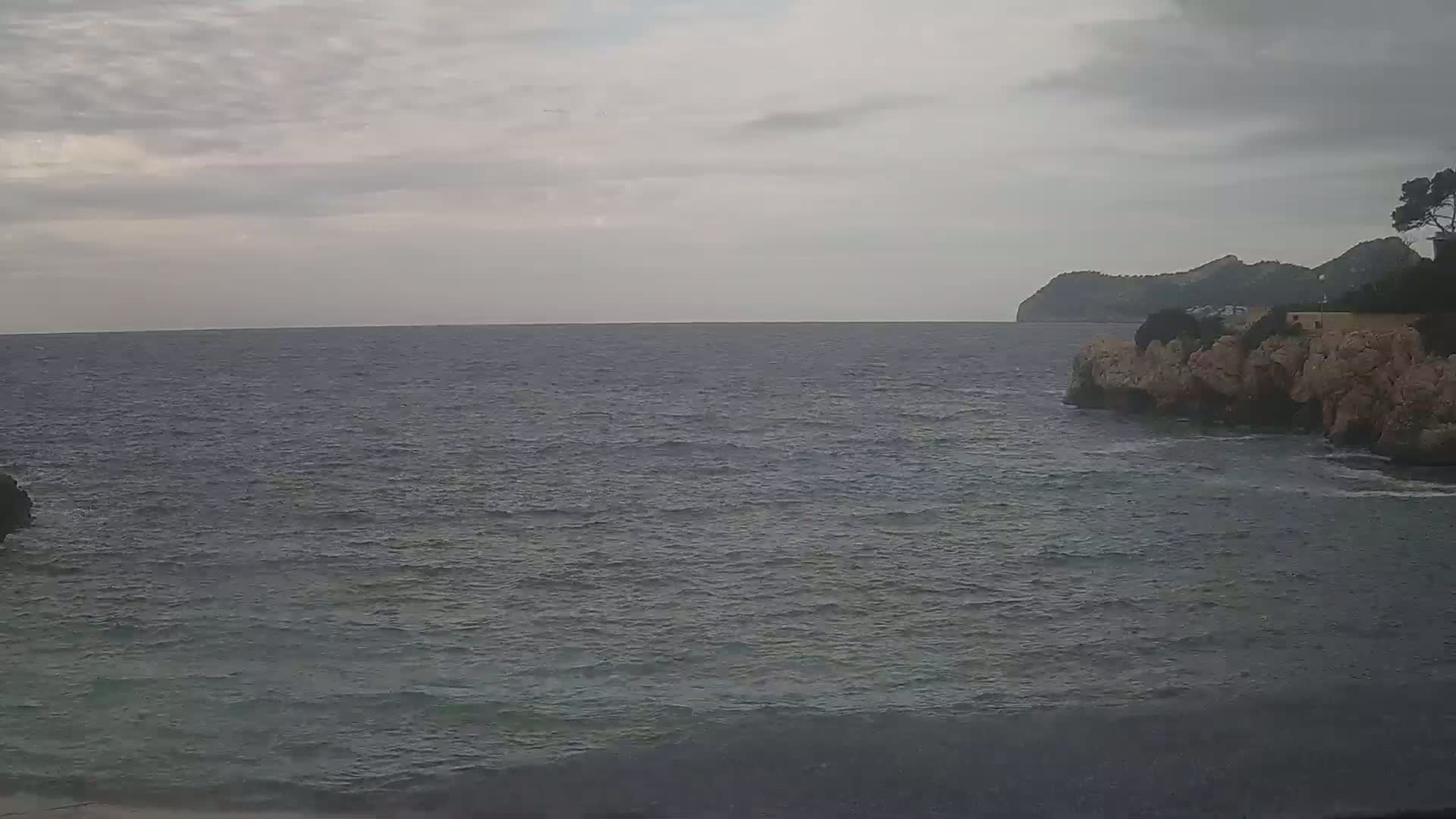 A rocky coast meets a calm, gray sea under a cloudy sky.