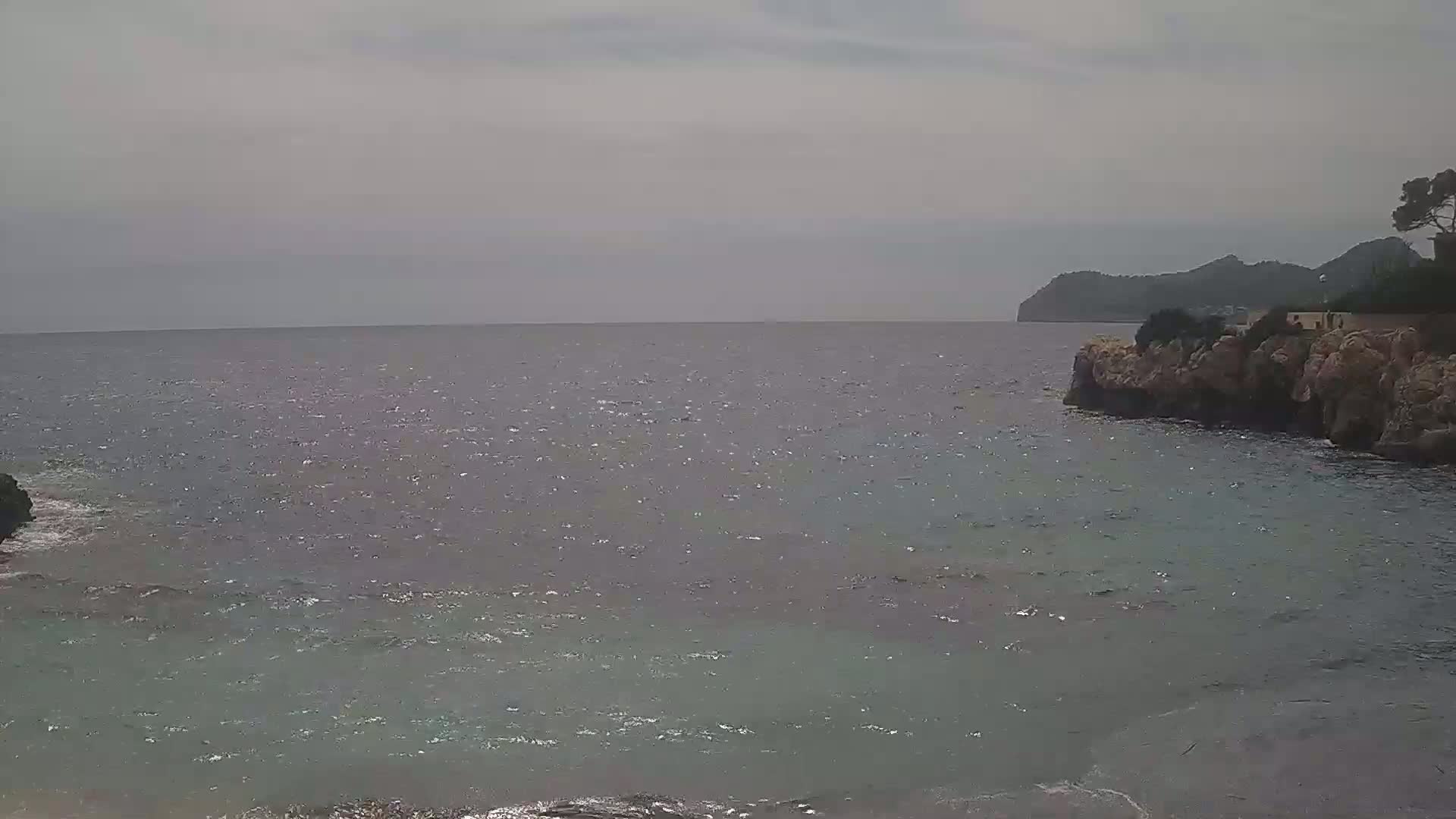A gently wavy sea laps against rocky shores under an overcast sky, with a distant landmass visible on the horizon.