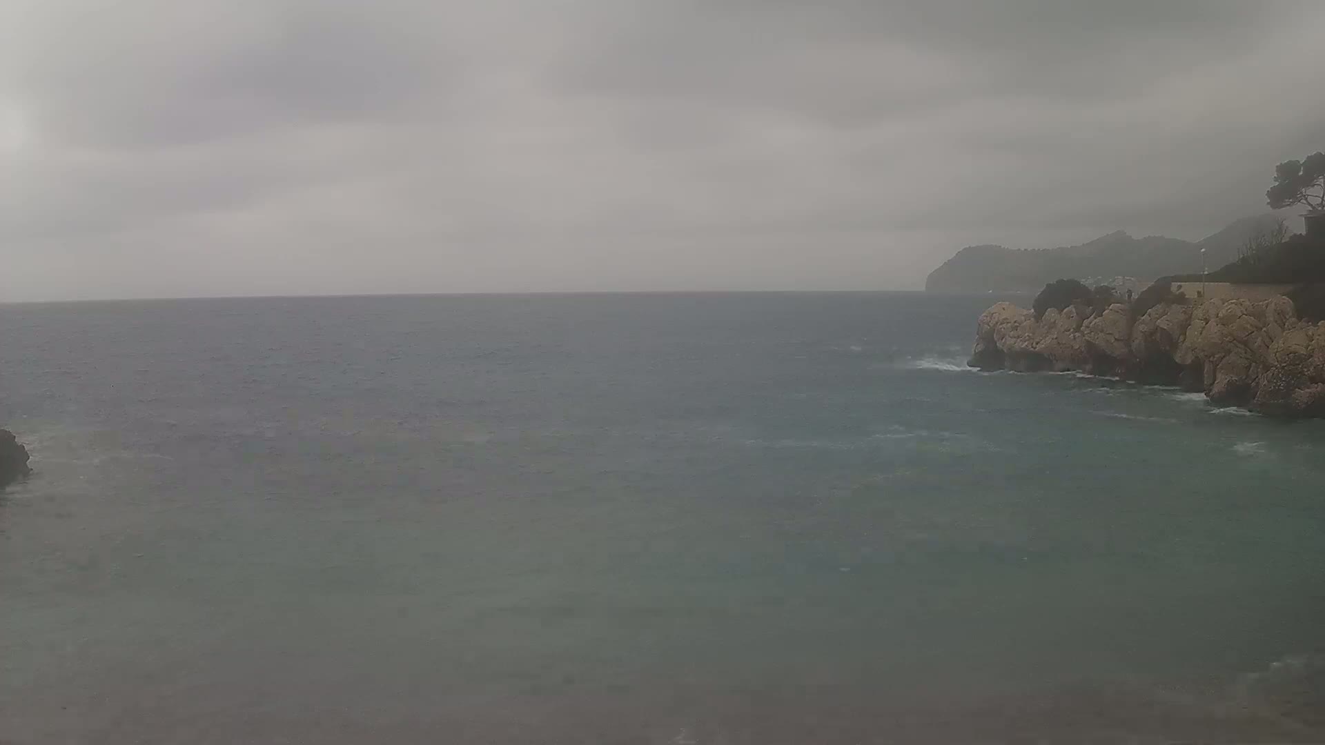A gray, overcast day shows a rocky coastline meeting a choppy sea under a cloudy sky.