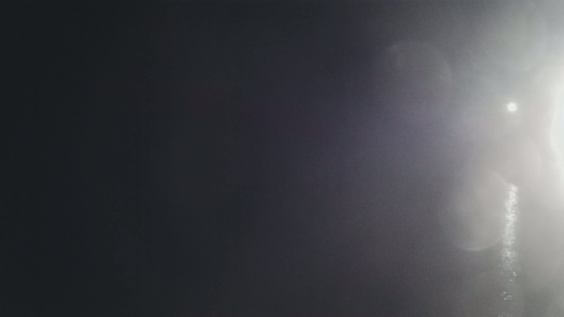 A bright light creates lens flare on a dark, mostly gray surface.
