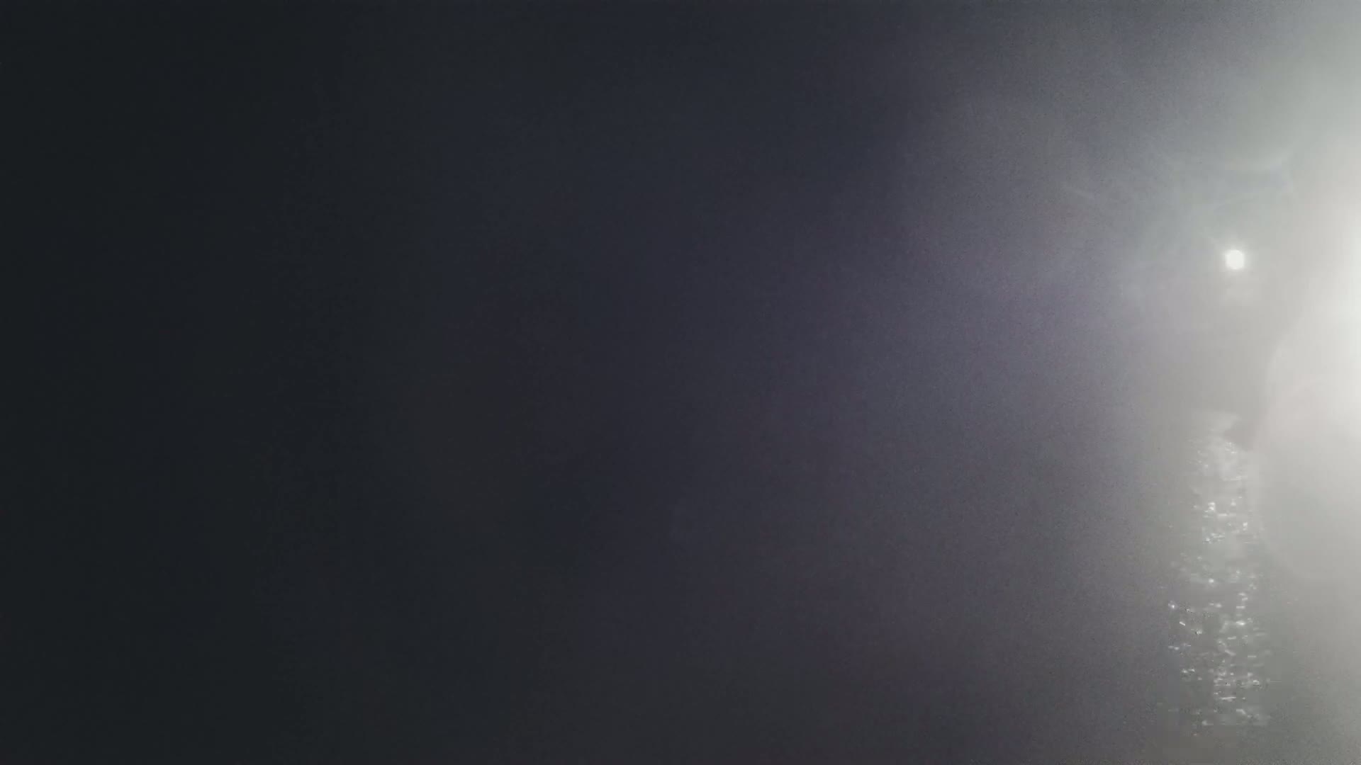 A blurry, dark image shows a bright light in the distance through a hazy or foggy atmosphere.