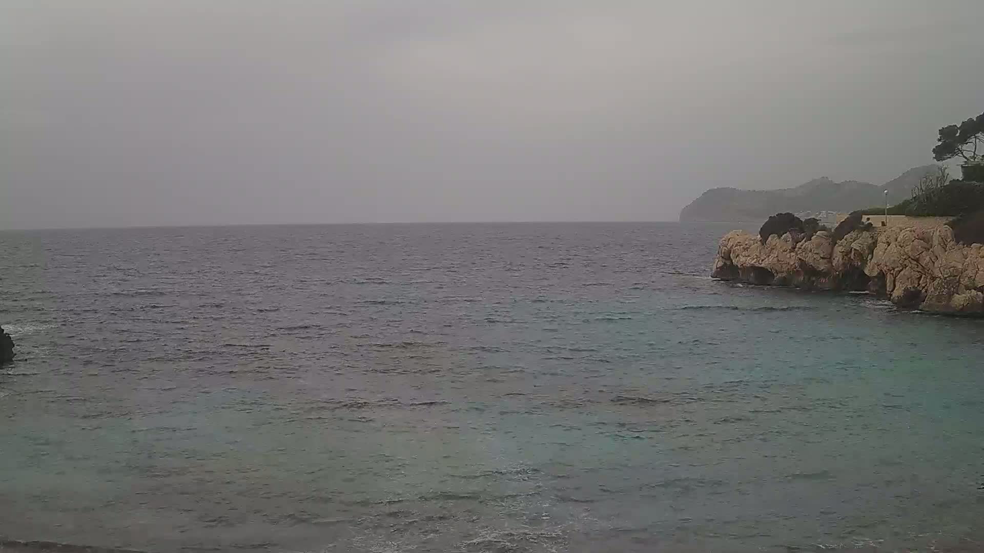 A calm, gray sea laps against a rocky shore under an overcast sky.